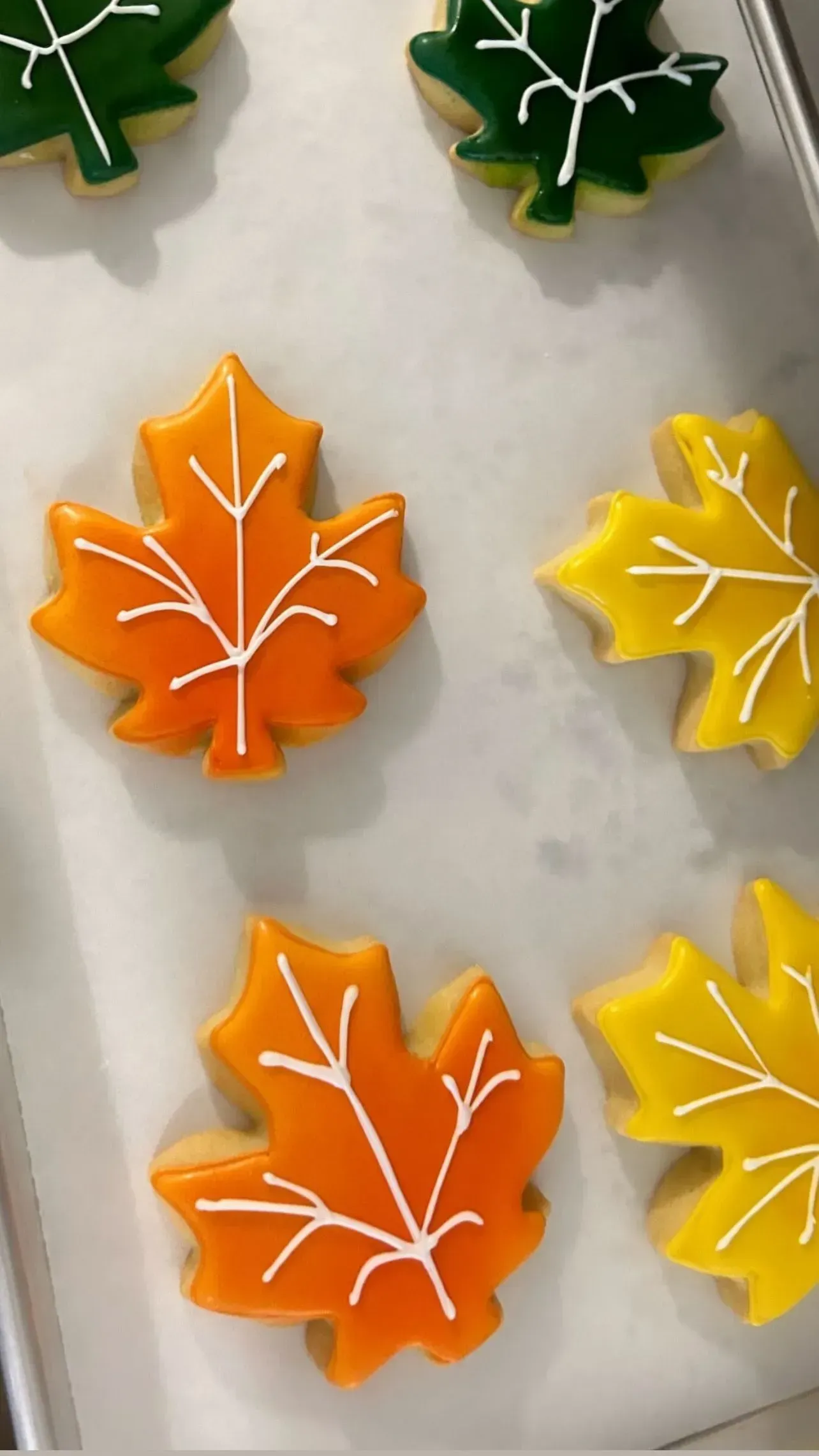 Leaf-shaped frosted cookies in green, orange, and yellow, arranged on a white surface.