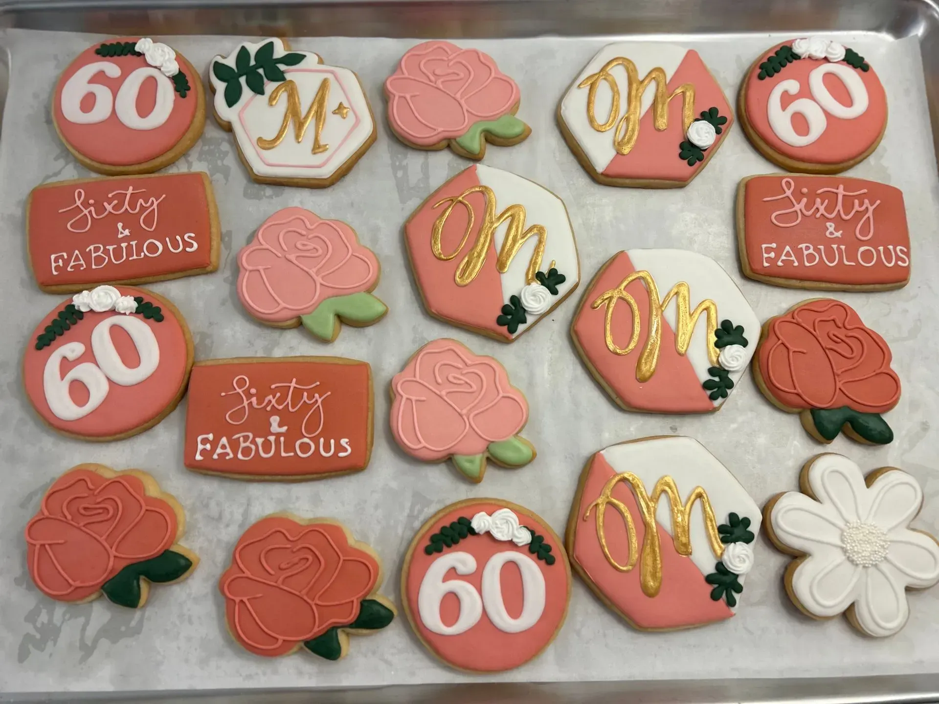 Assorted pink, coral, white and gold decorated cookies spelling “60” and “birthday fabulous” on a tray