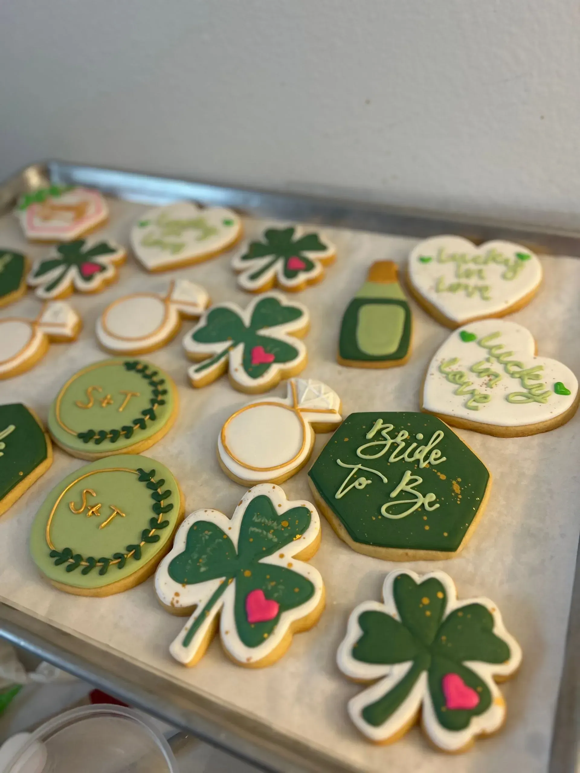Assorted green, white, and gold shamrock and heart-shaped decorated cookies on a tray.