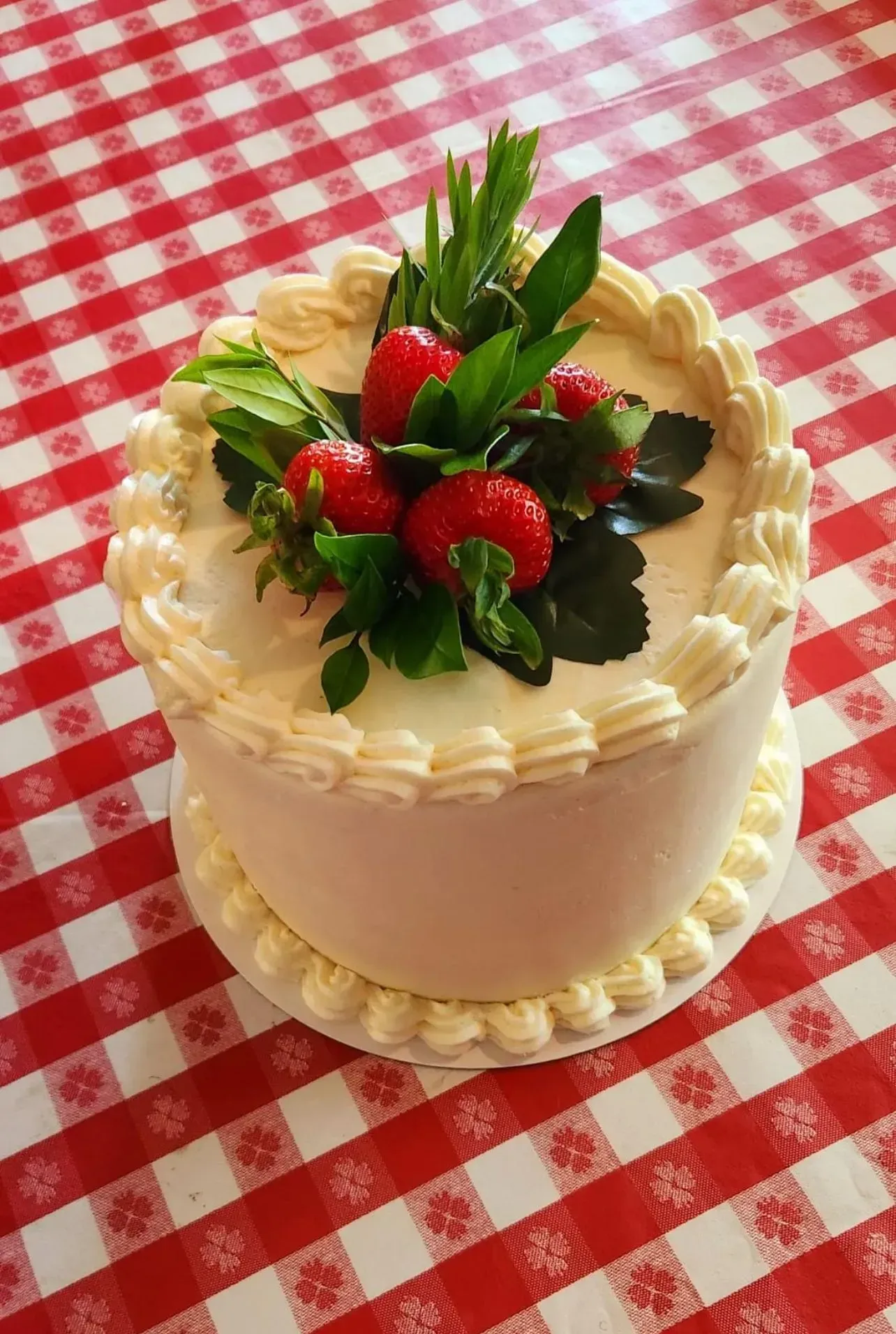 Small frosted cake topped with strawberries on a red-and-white checkered tablecloth