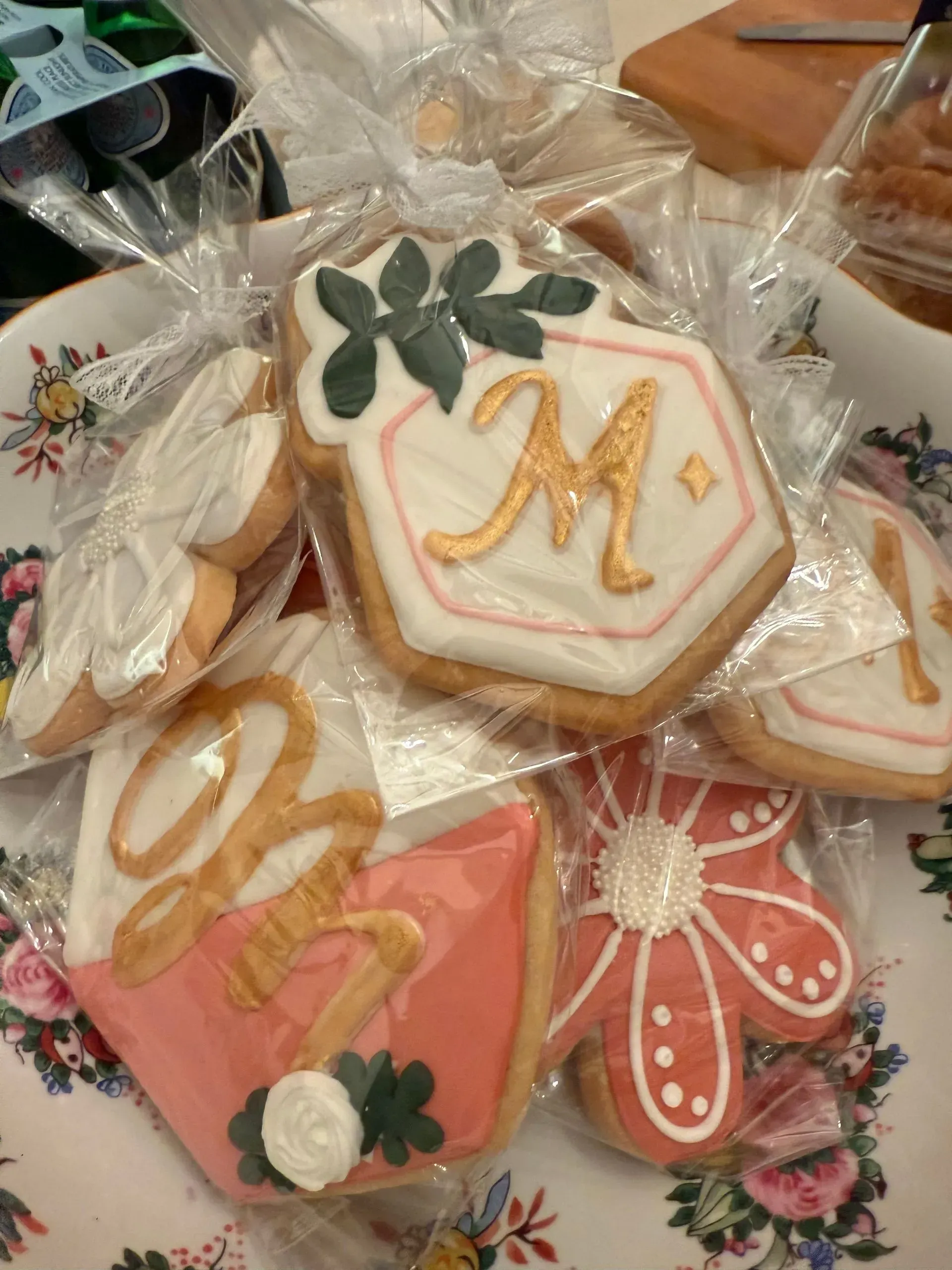 Assorted decorated flower and monogram cookies wrapped in clear bags on a floral surface