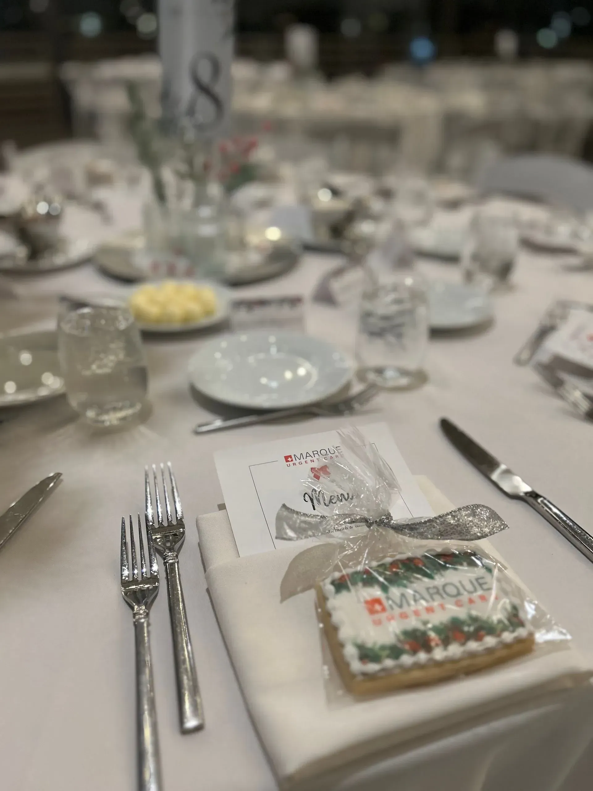 Elegant banquet table set with white linens, glassware, silverware, and a frosted dessert plate at each place setting