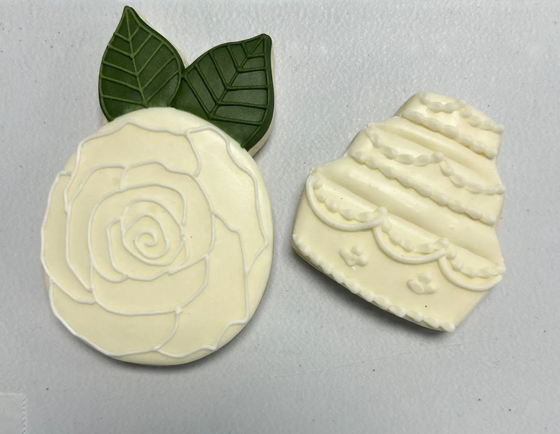 Two cream-colored decorative soaps or cookies, one with rose petals and leaves, one with layered swirl design