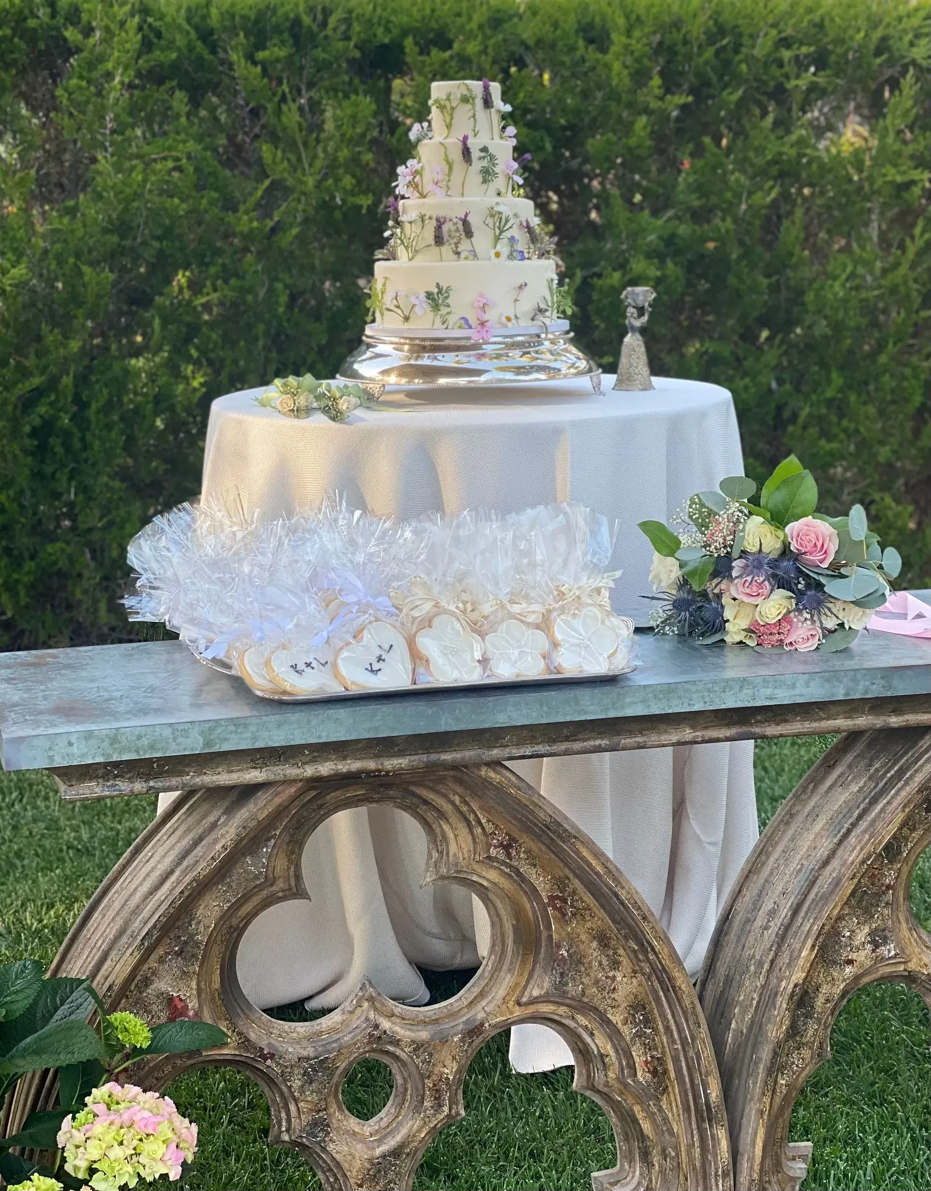 Elegant white tiered wedding cake on a rustic table with floral arrangements outdoors