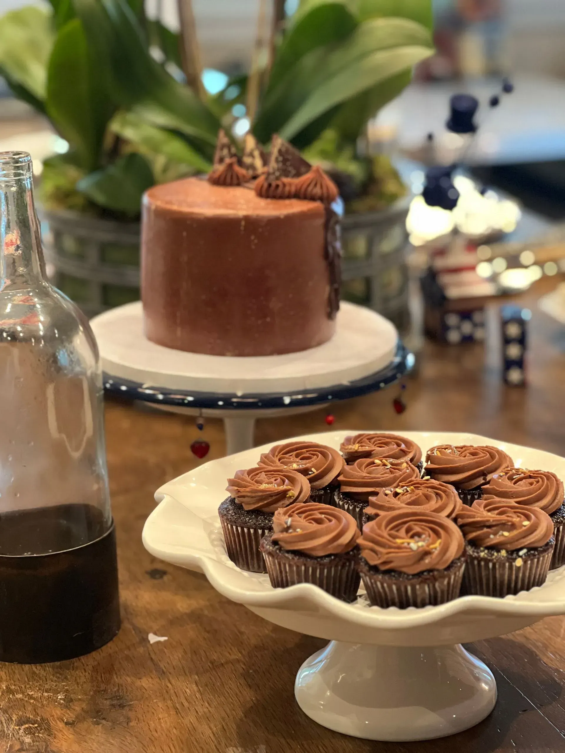 Dessert table with chocolate cake and a plate of frosted cupcakes on a white pedestal stand
