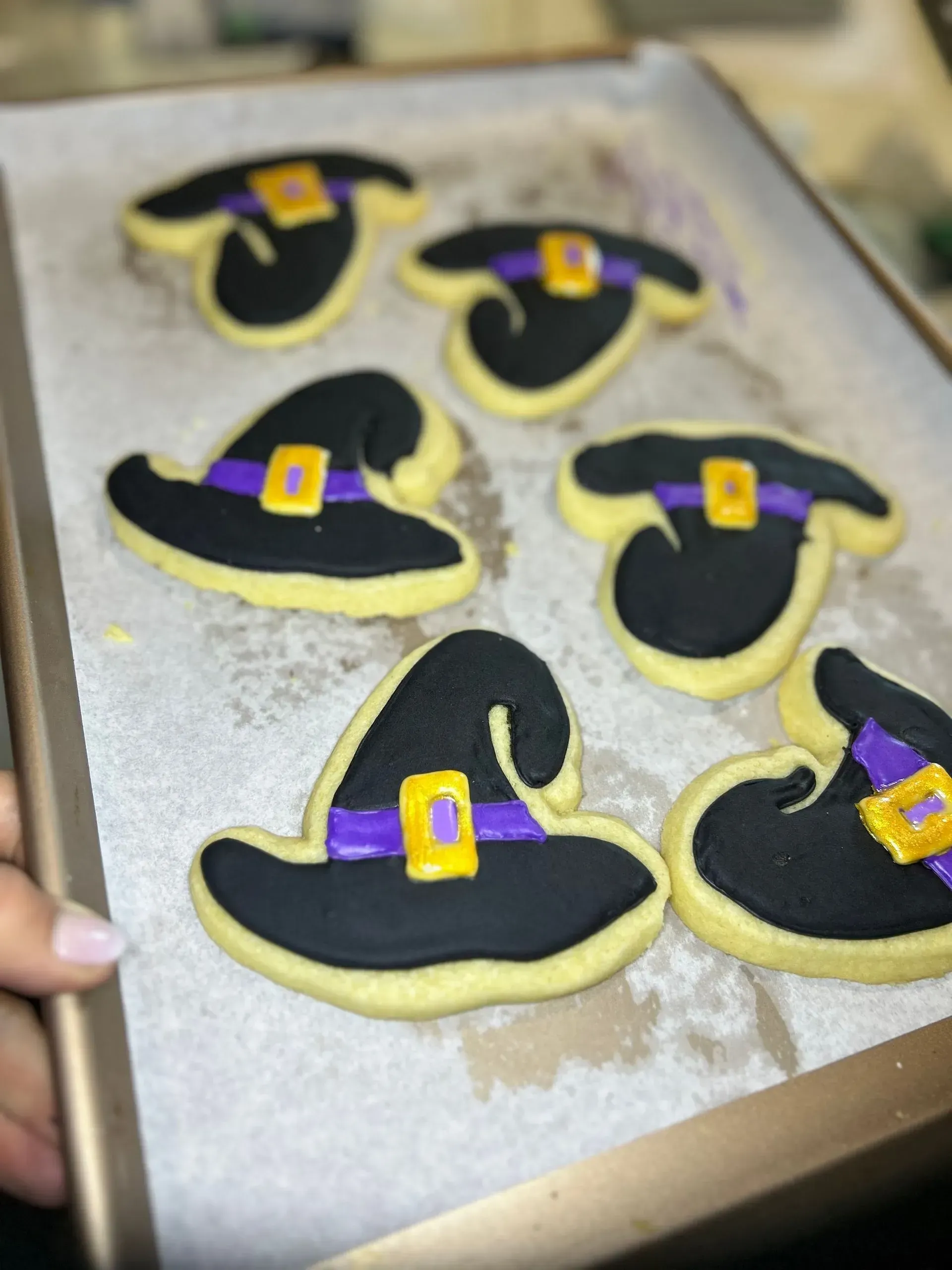 Halloween witch hat cookies on a baking sheet, black with yellow moons and purple bands
