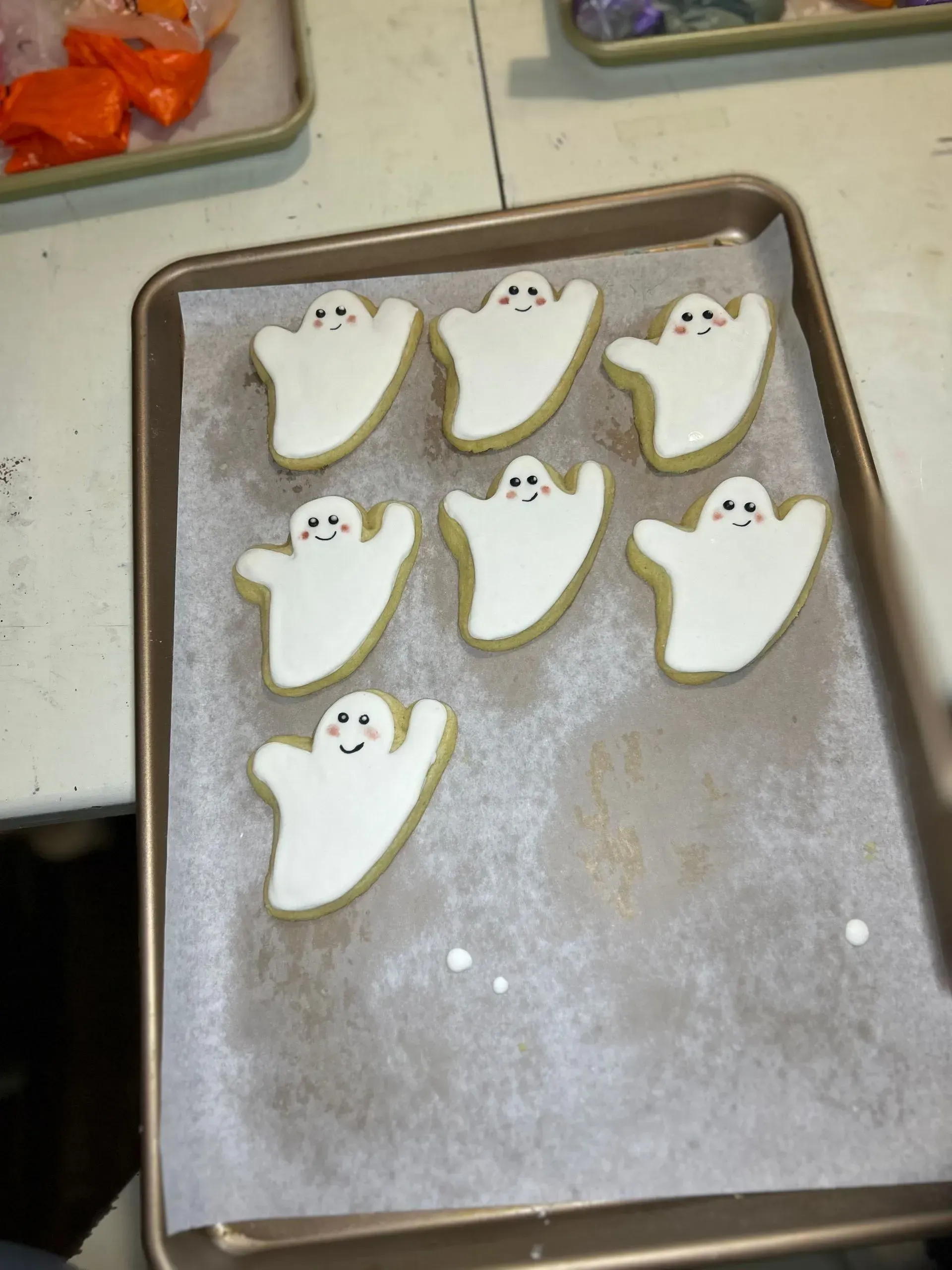 Ghost-shaped cookies on a baking sheet, with orange candy pieces in the background