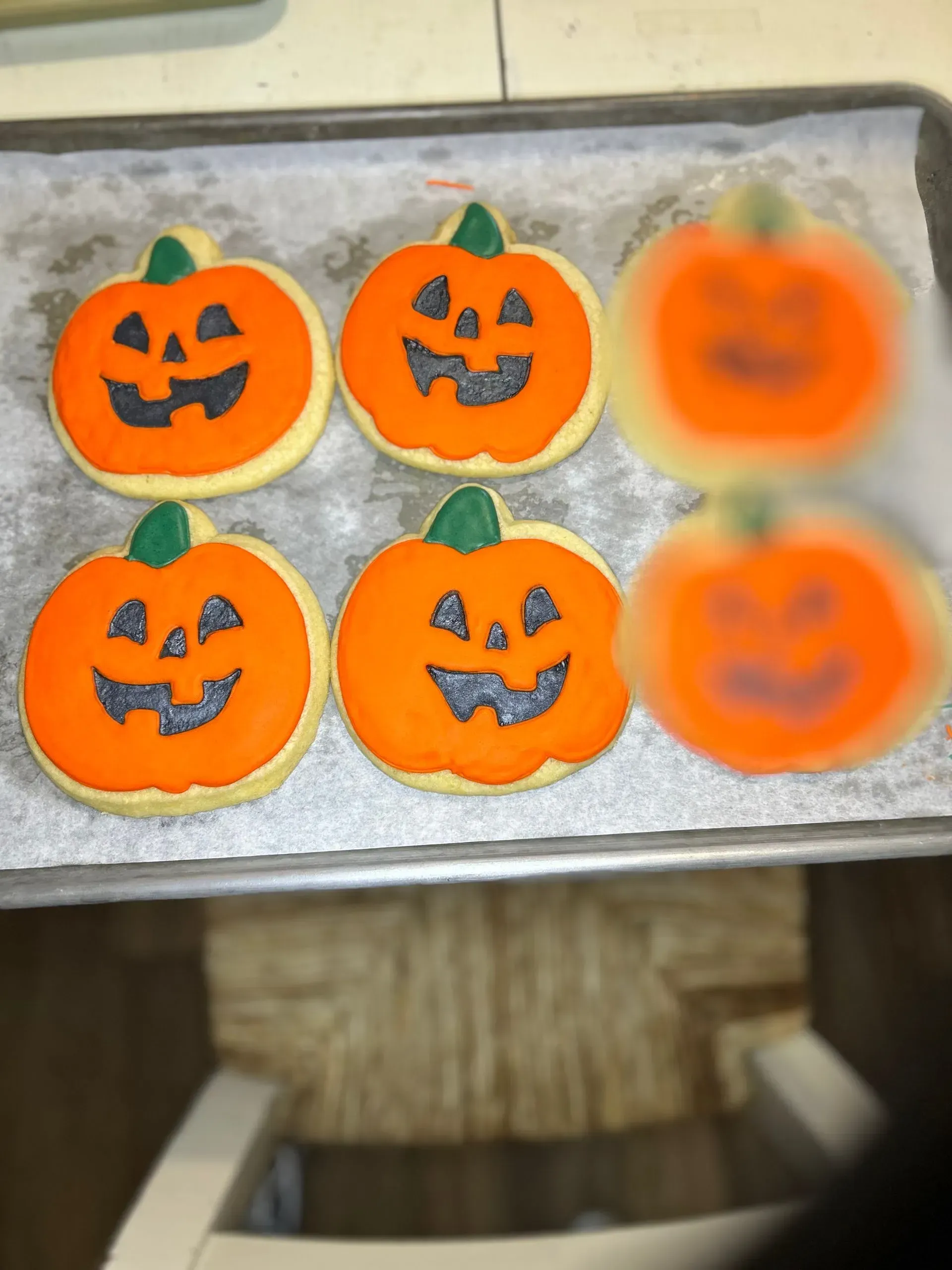 Tray of pumpkin-shaped Halloween cookies, four decorated and two blurred out