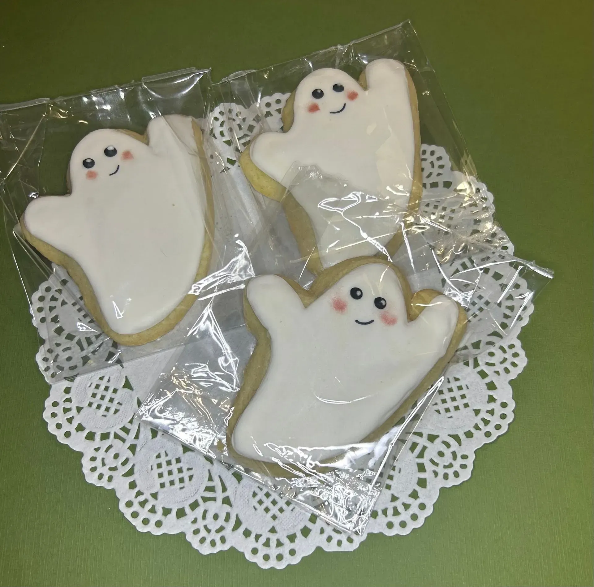Three ghost-shaped iced cookies with smiling faces on a lace doily