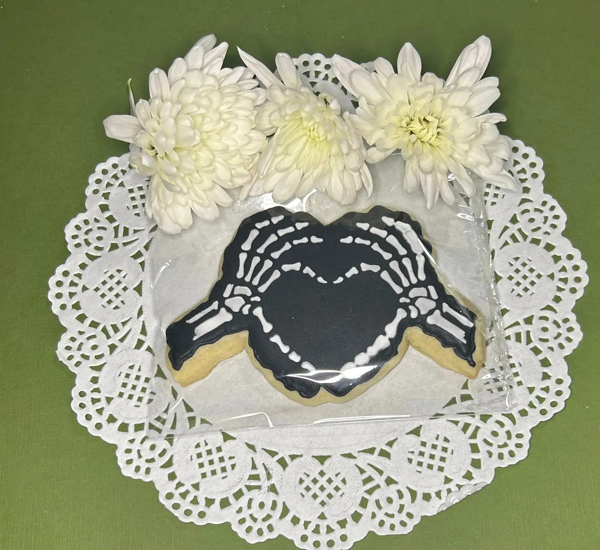 Decorative black turtle cookie on a white doily with white flowers on a green background