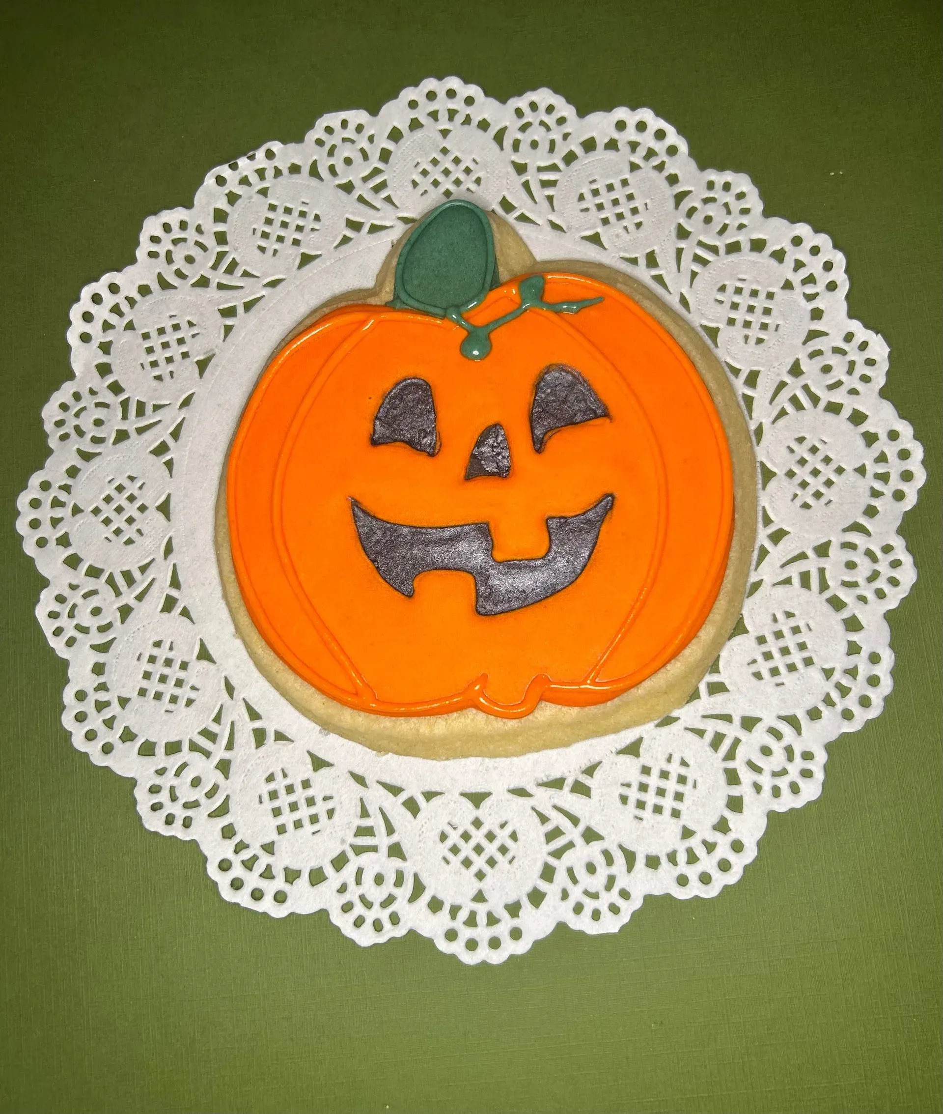 Orange jack-o'-lantern cookie on a white lace doily against a green background