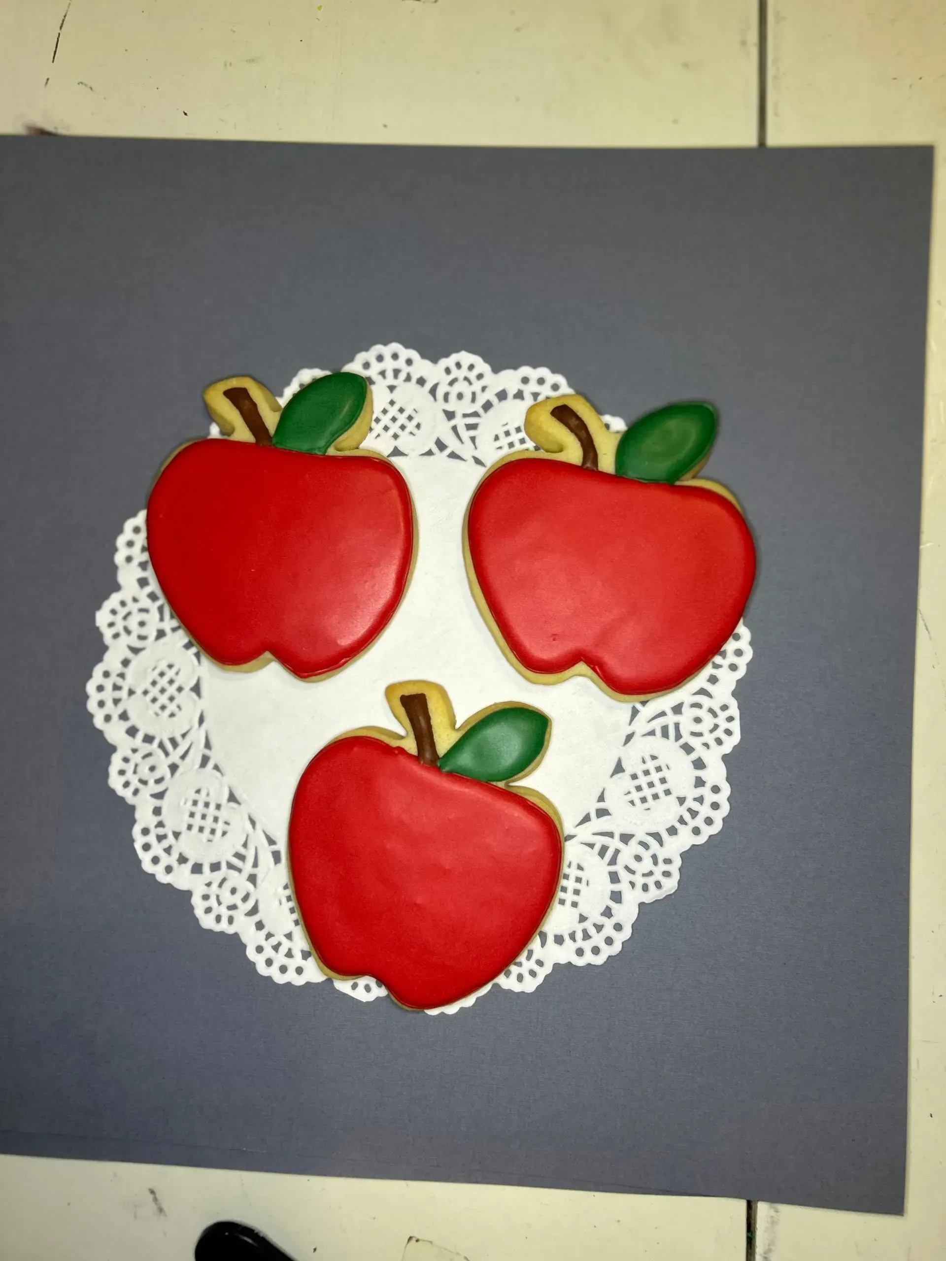 Three red apples on a white lace doily against a dark gray background.