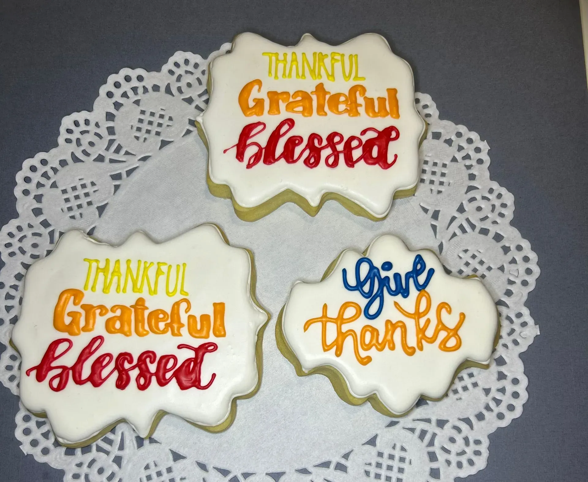 Three decorated cookies on a white doily with “Thankful, Grateful, Blessed” and “give thanks” icing text