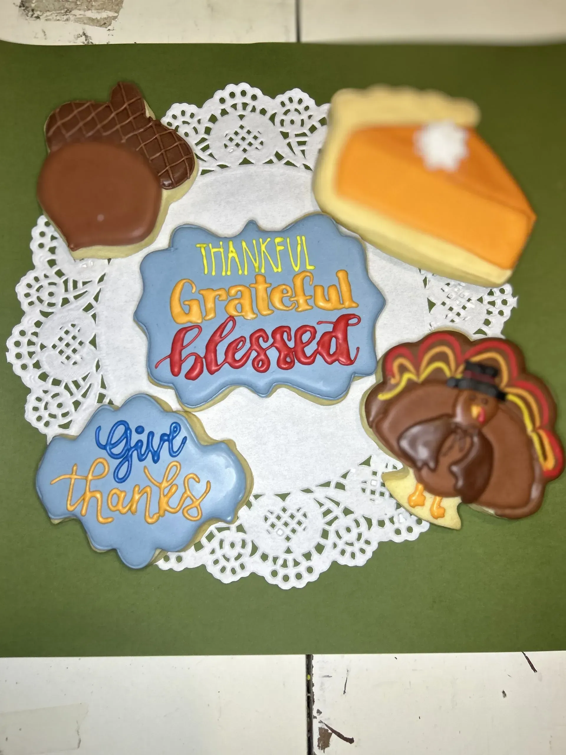 Thanksgiving cookies on a lace doily: “Thankful Grateful Blessed” and “Give thanks” designs with acorns and pumpkin pie.