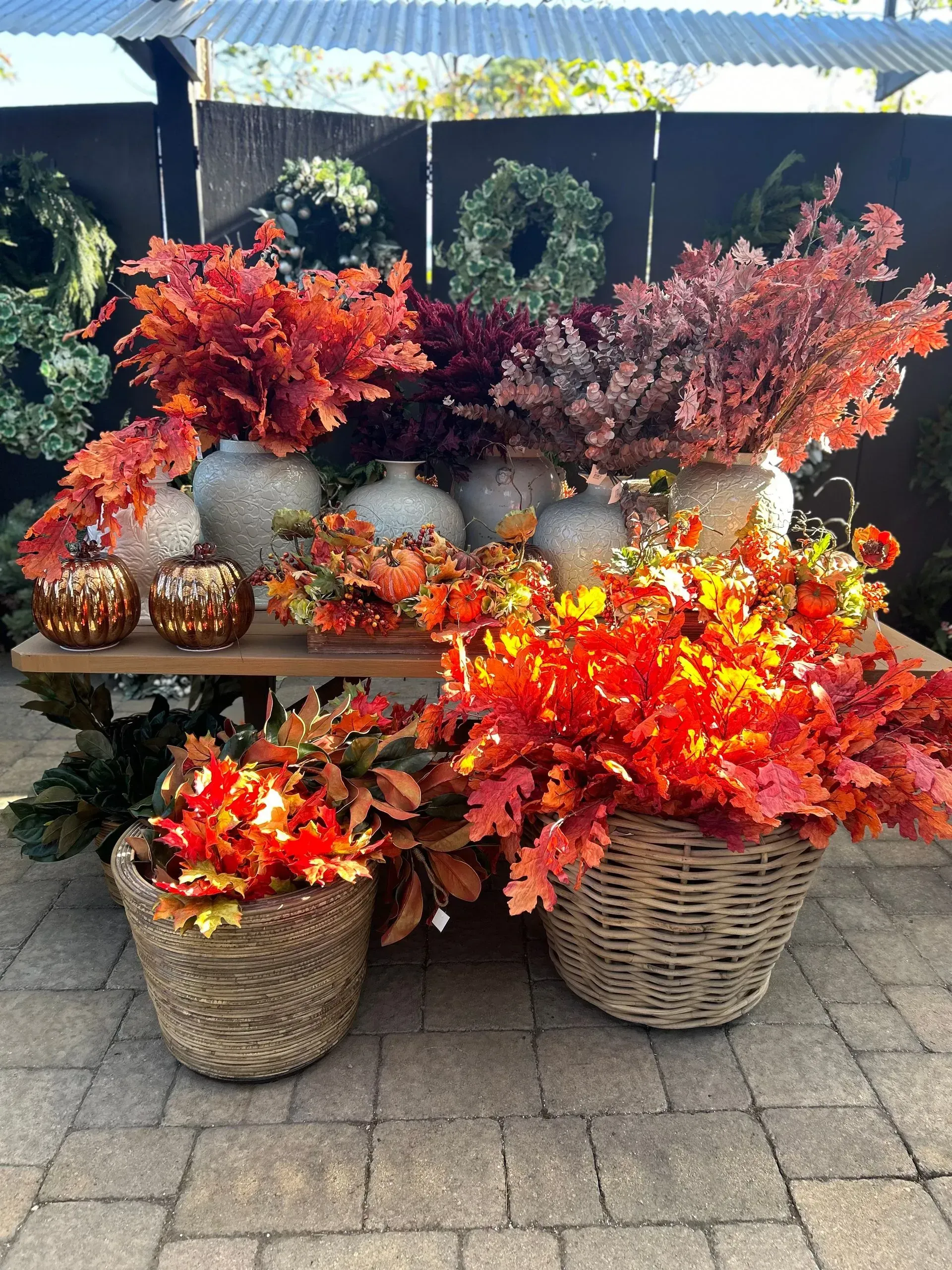 Fall decor with red, orange, and purple faux foliage in baskets and pumpkins on a display bench