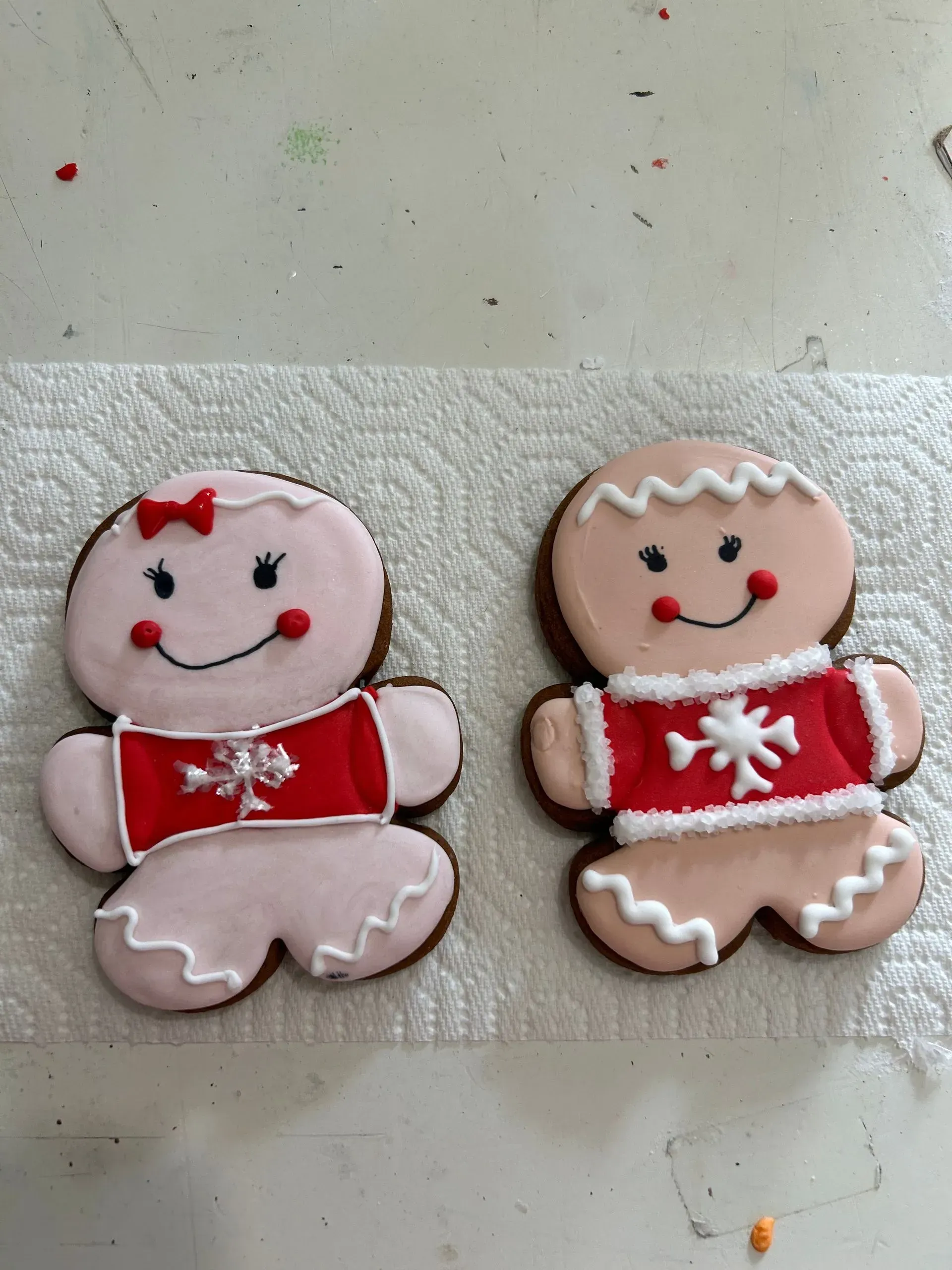 Two gingerbread cookies decorated with white icing, red bows, and smiling faces on a paper towel.