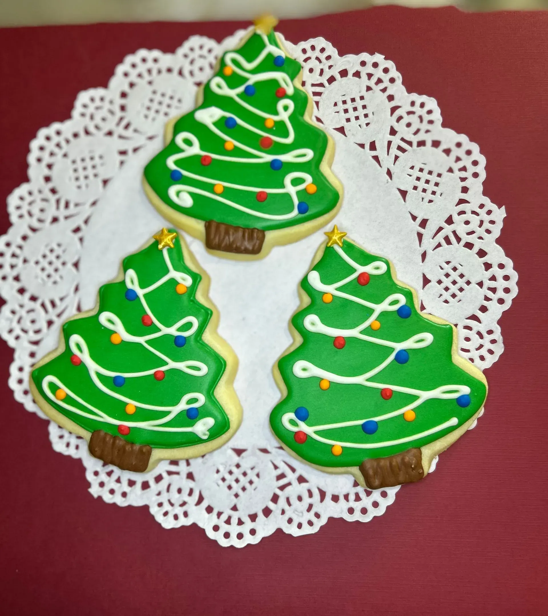 Three decorated Christmas tree cookies on a white lace doily against a red background