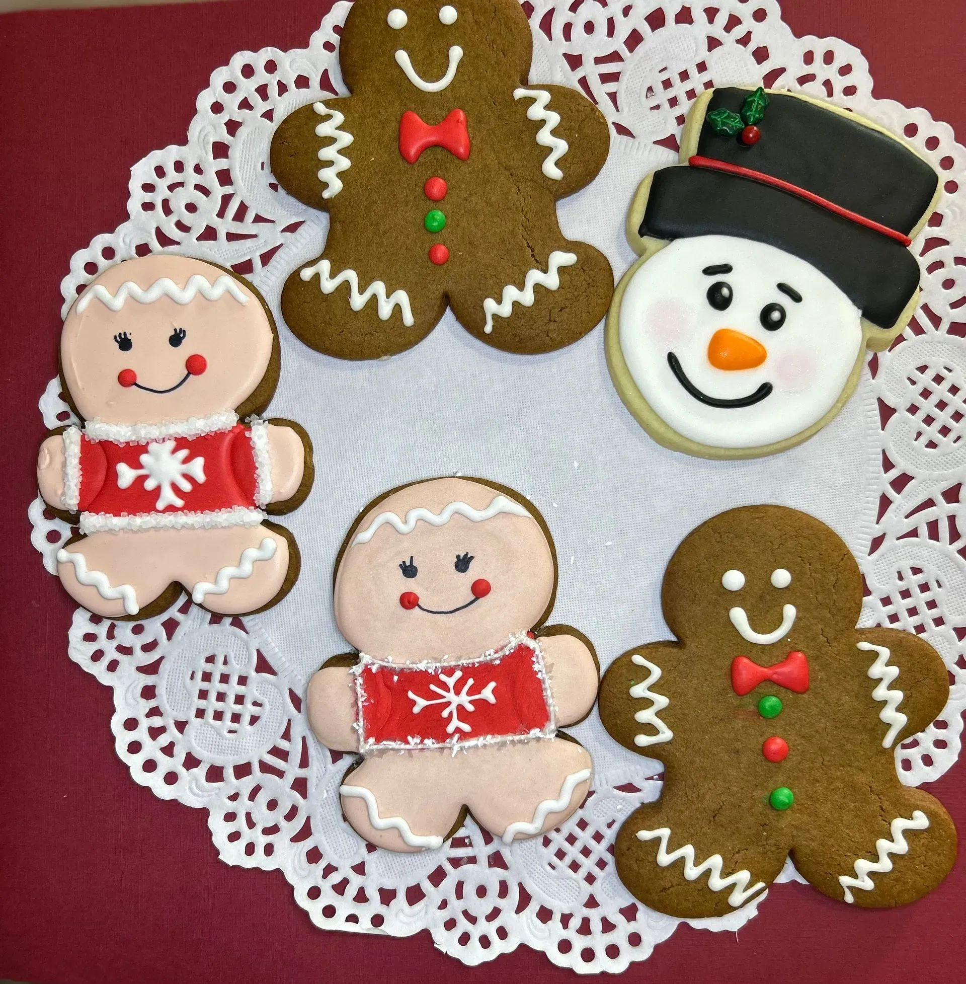 Gingerbread cookies and a snowman cookie on a white lace doily, with red and green icing decorations.