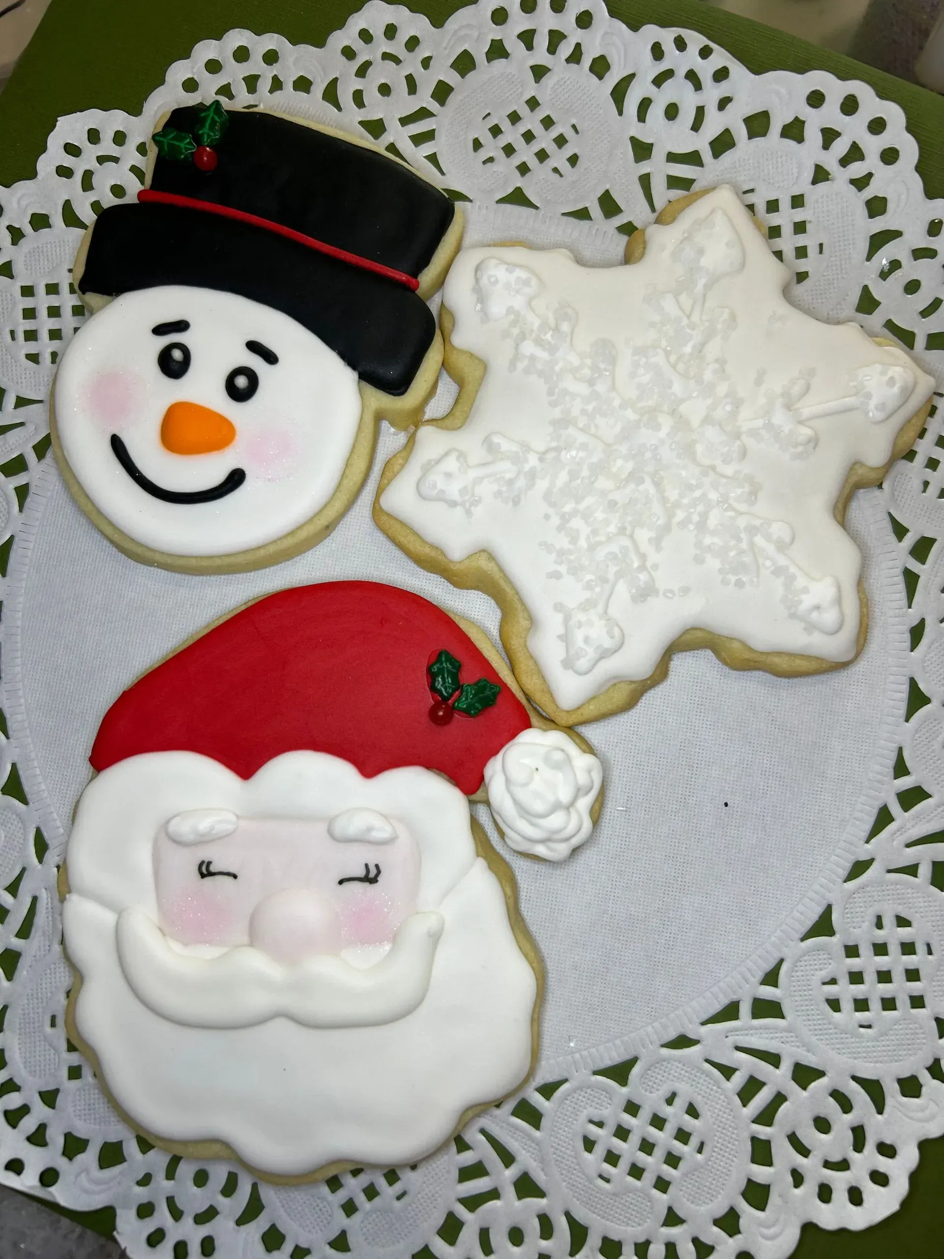 Snowman, Santa hat cookie, and snowflake-shaped cookie on a lace doily