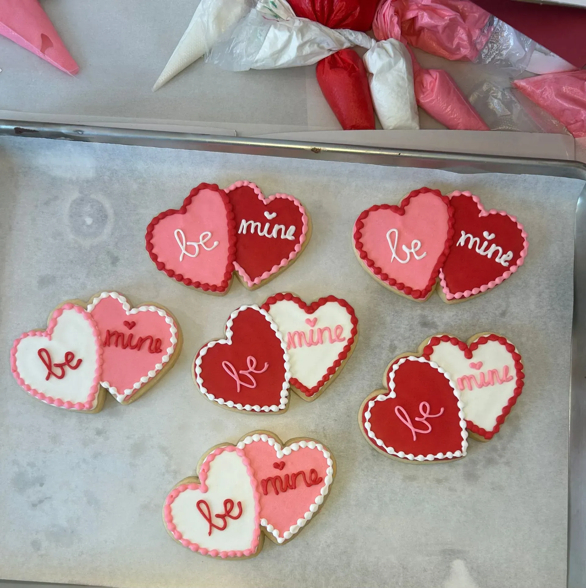 Heart-shaped cookies with red, pink, and white icing reading “be mine” on a baking tray