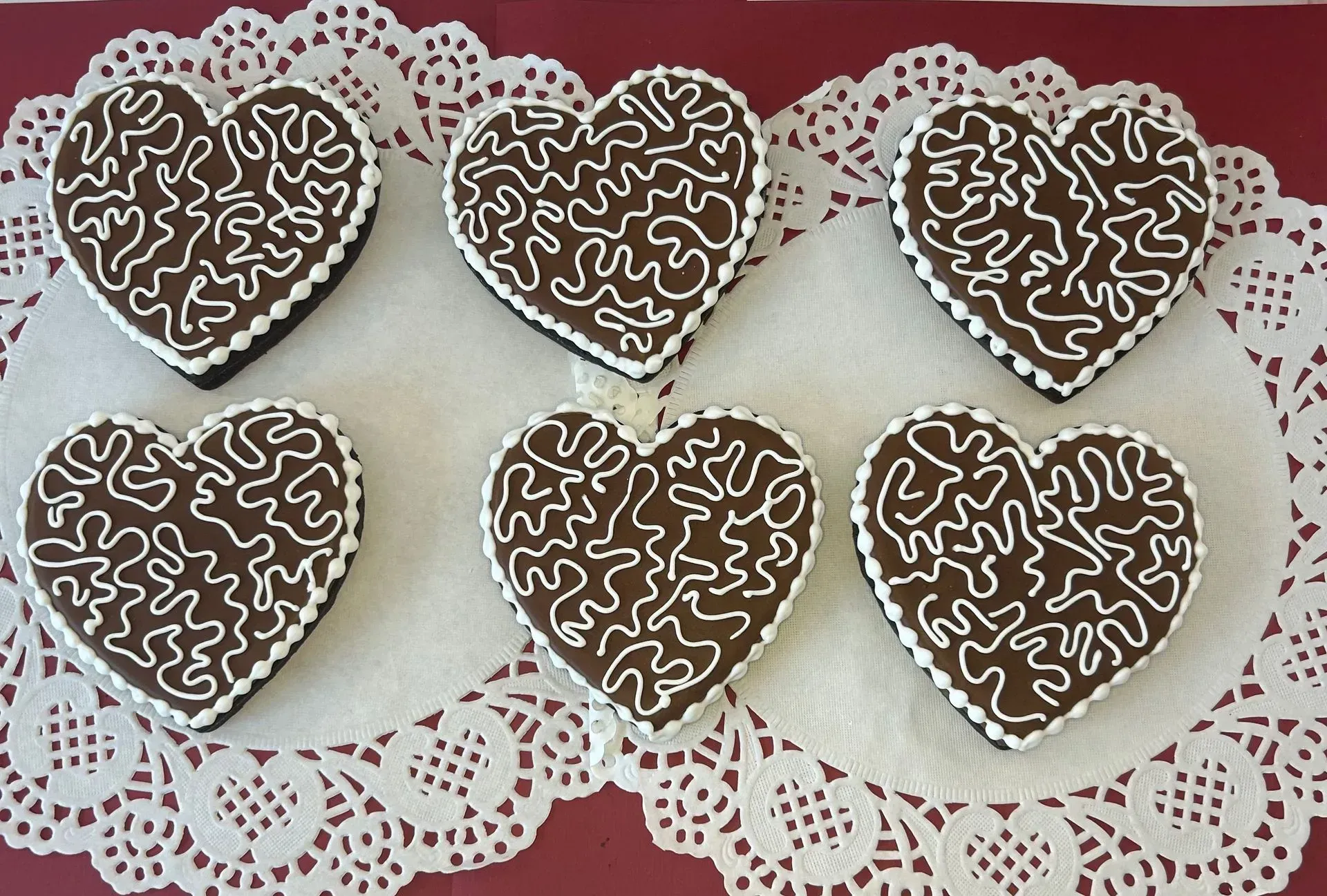 Six chocolate heart cookies with white icing on lace doilies