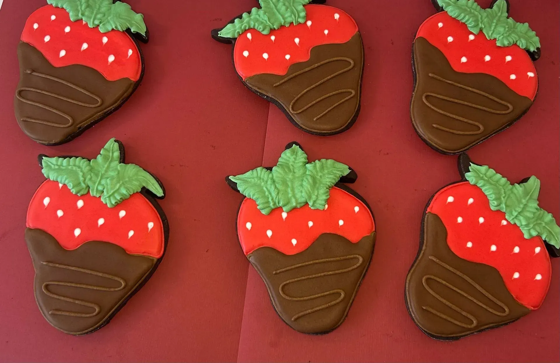 Six chocolate-covered strawberry cookies on a red surface