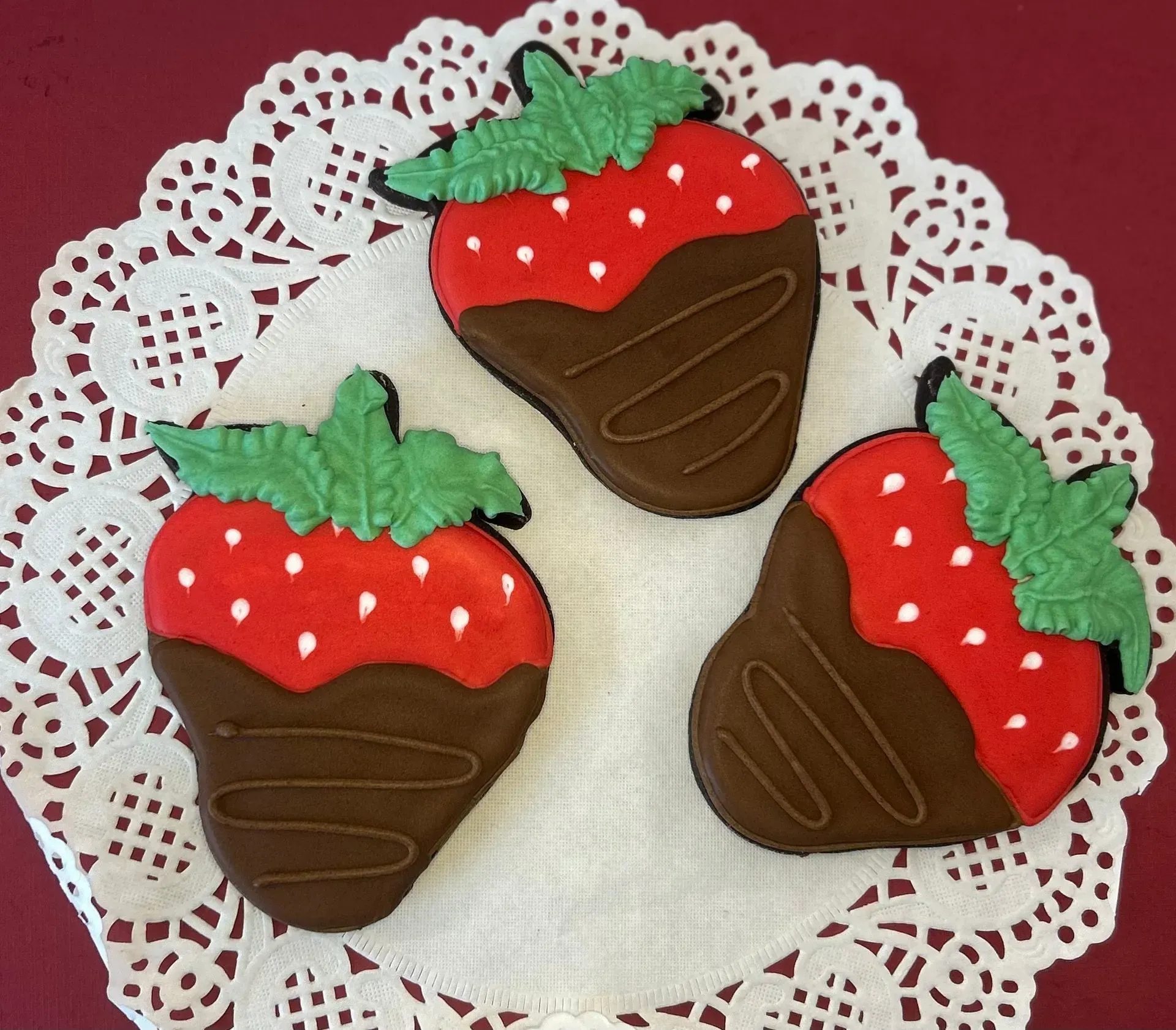 Three chocolate-dipped strawberry cookies on a white lace doily