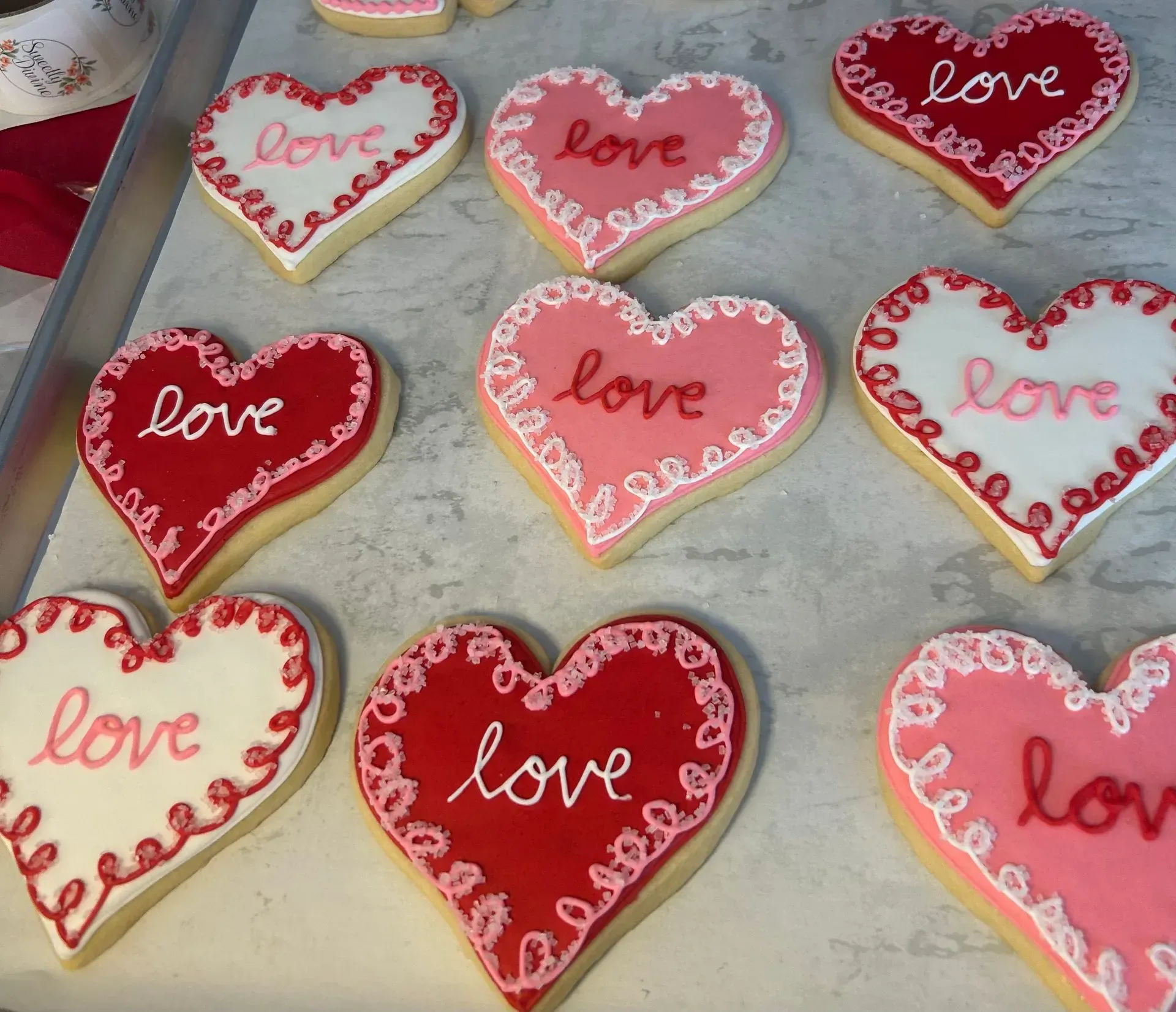 Heart-shaped love cookies iced in pink, red, and white on a baking tray