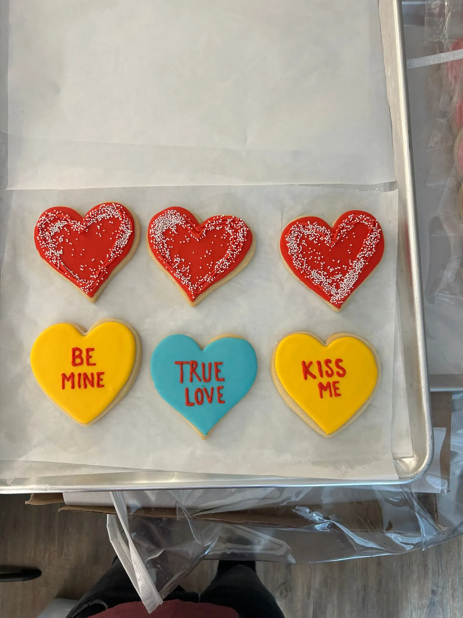 Valentine’s candy hearts on a tray: three red hearts and three pastel hearts with “Be Mine,” “True Love,” and “Kiss Me”