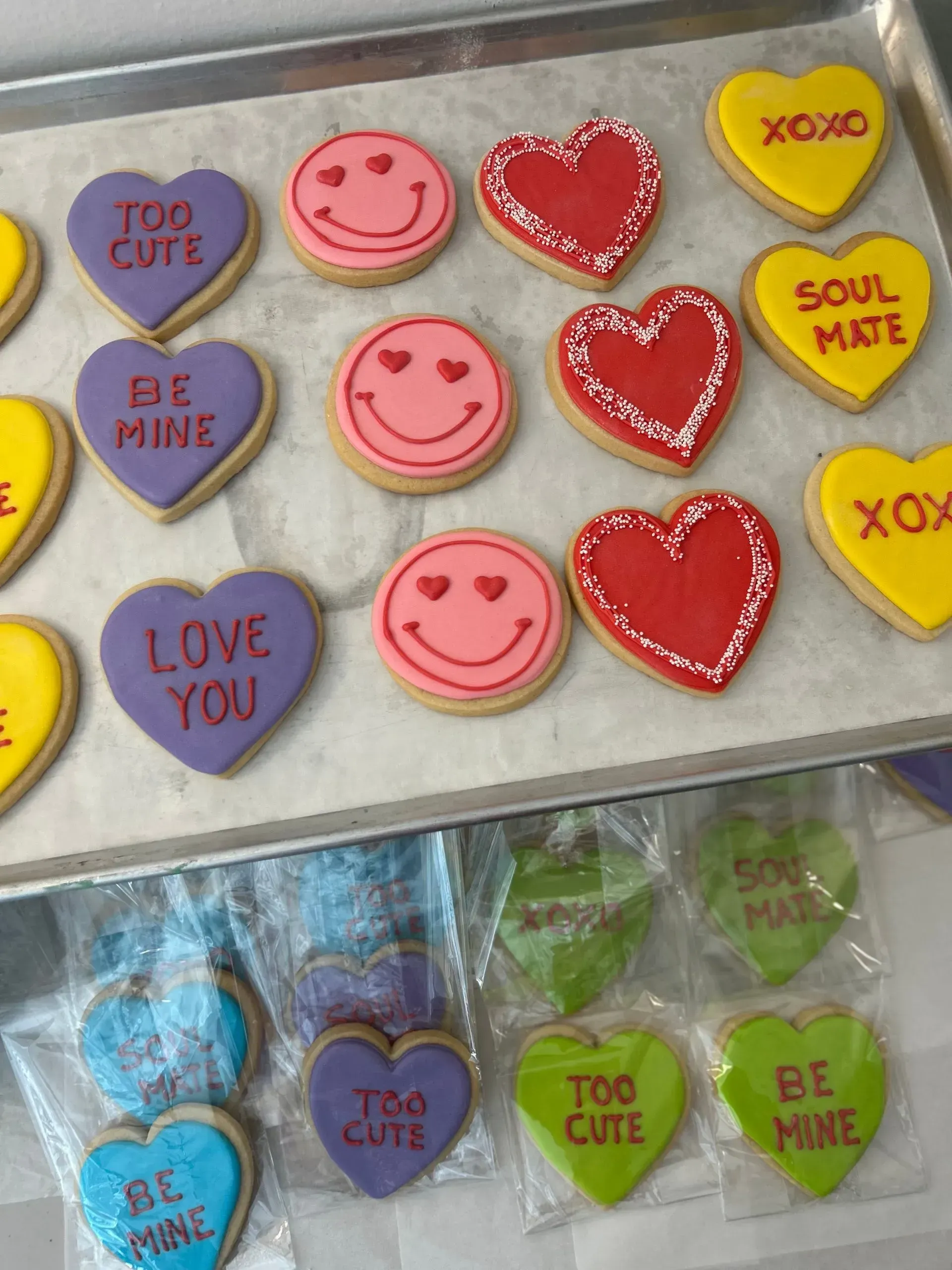 Heart and smiley-face decorated cookies in pink, red, yellow, and blue on a tray and in a package.
