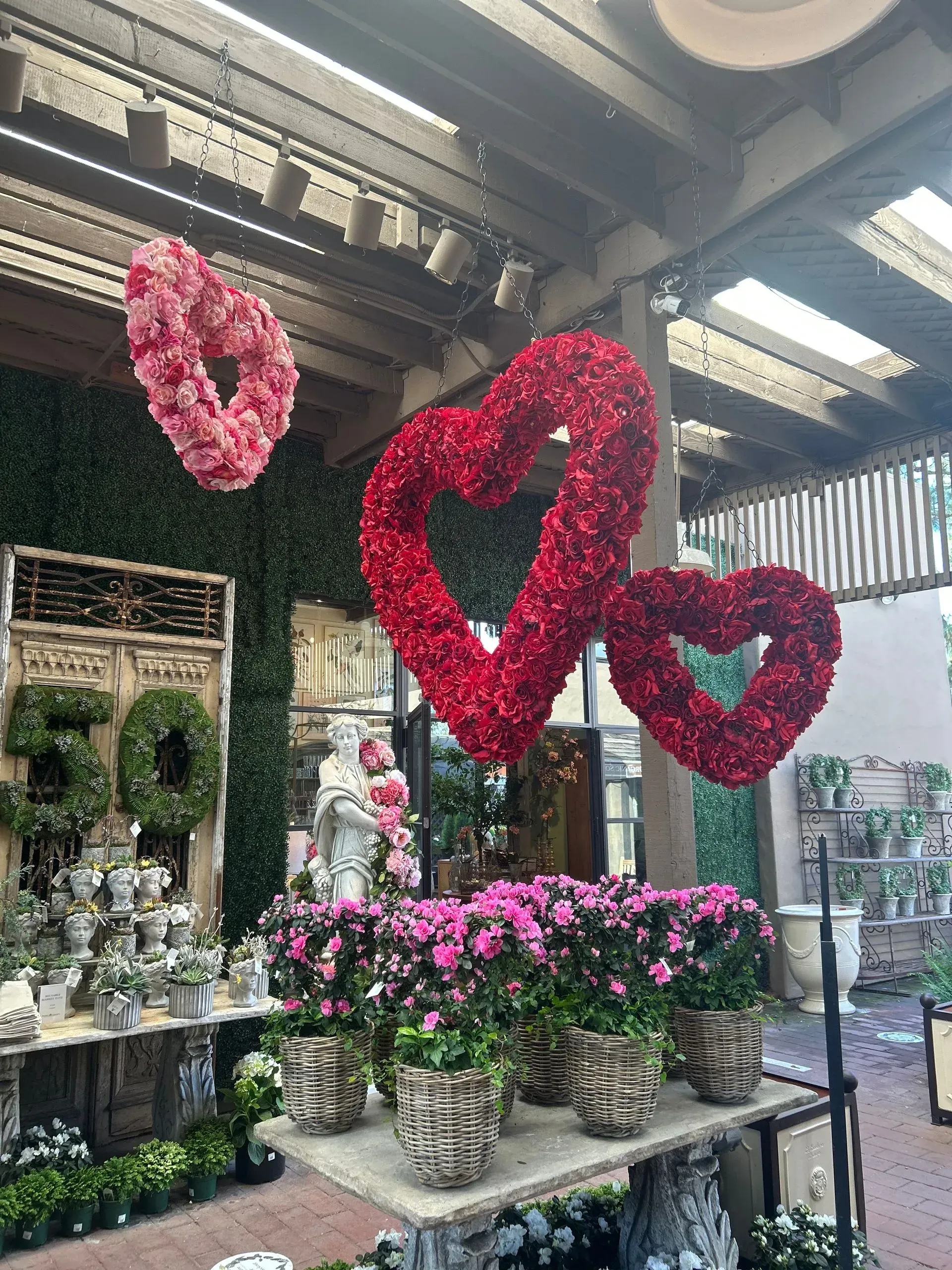 Flower shop display with pink floral heart decorations and potted blooms under a covered outdoor area