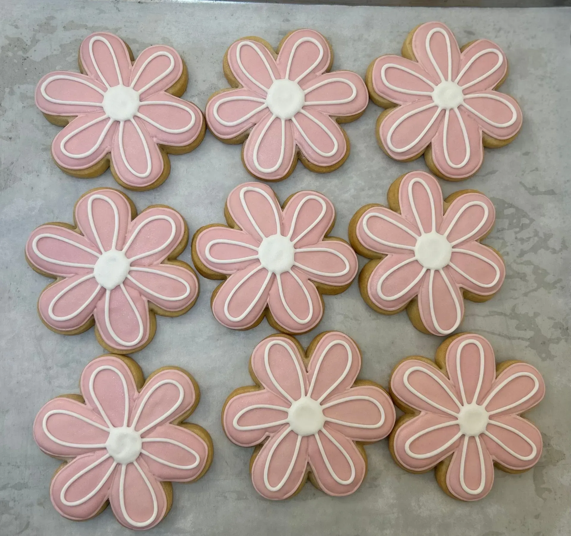 Nine pink flower-shaped cookies with white icing centers on a gray surface.