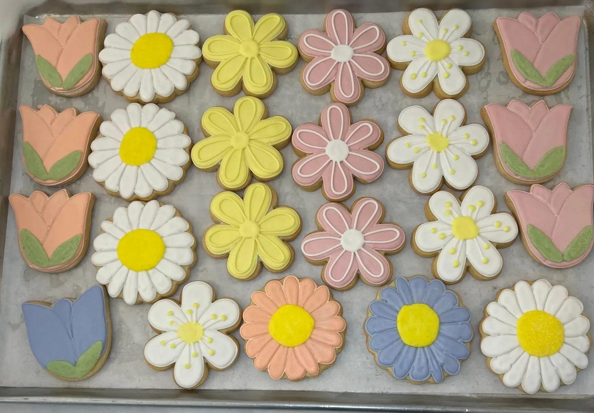 Pastel flower-shaped cookies arranged in rows on a tray