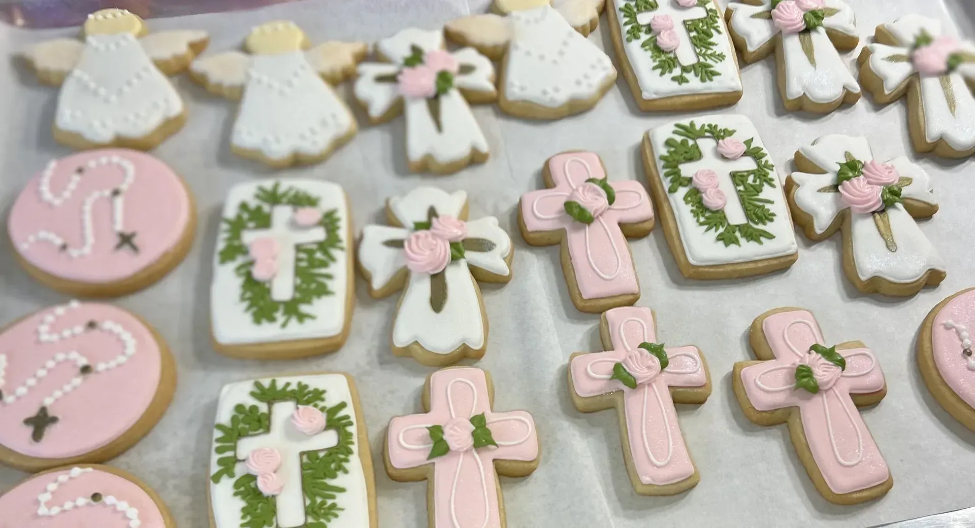 Pastel iced cookies shaped like crosses, circles, and dresses on a light surface