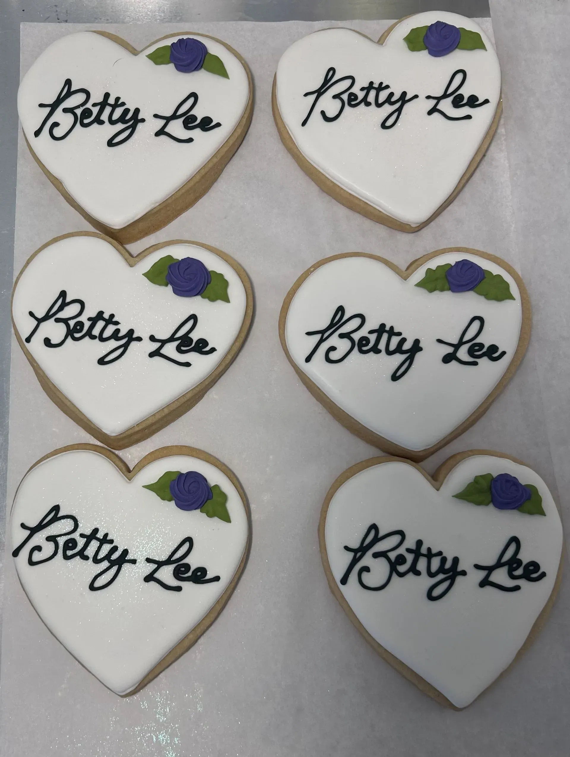 Heart-shaped Betty Lee cookies with white icing and purple and green accents arranged in rows