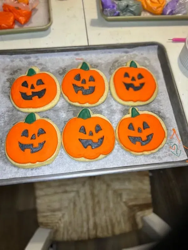 Six orange frosted pumpkin cookies with jack-o'-lantern faces on a baking sheet