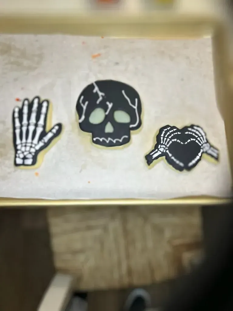 Three stickers: skeletal hand, cracked black skull, and skeletal heart on a beige surface