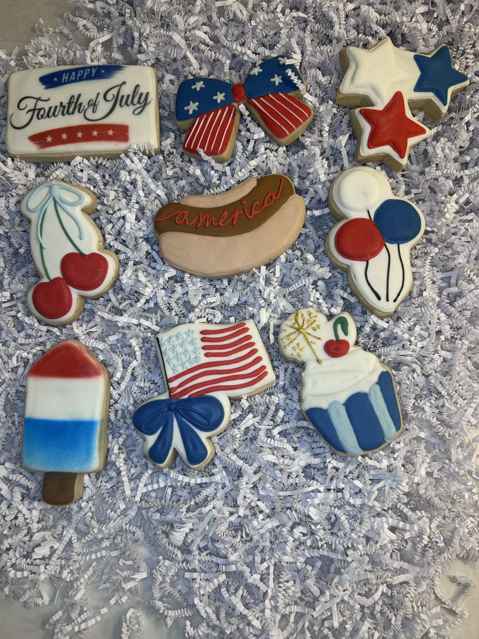 Fourth of July decorated cookies: flag, star, fireworks, popsicle, and balloon designs on gray fur background