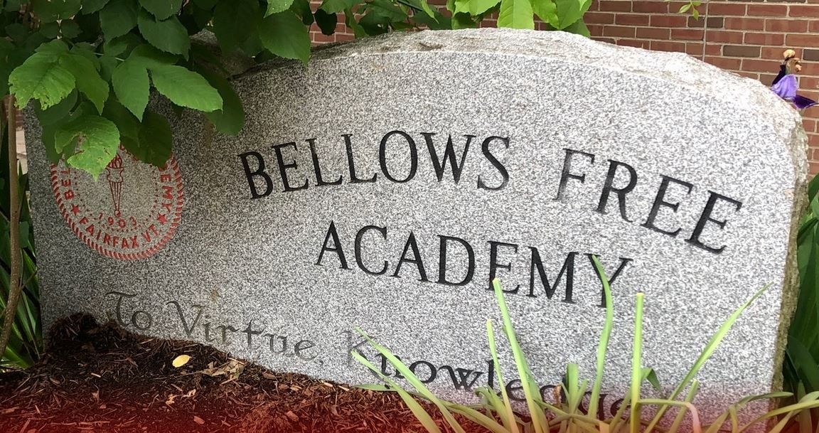 A large stone sign for bellows free academy is sitting in front of a brick building.