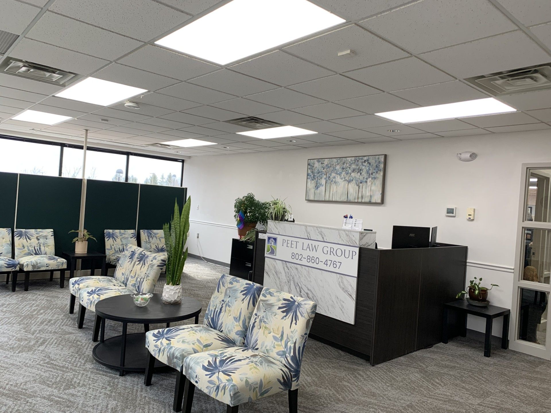 A real estate office's waiting room with chairs , tables , and a reception desk.
