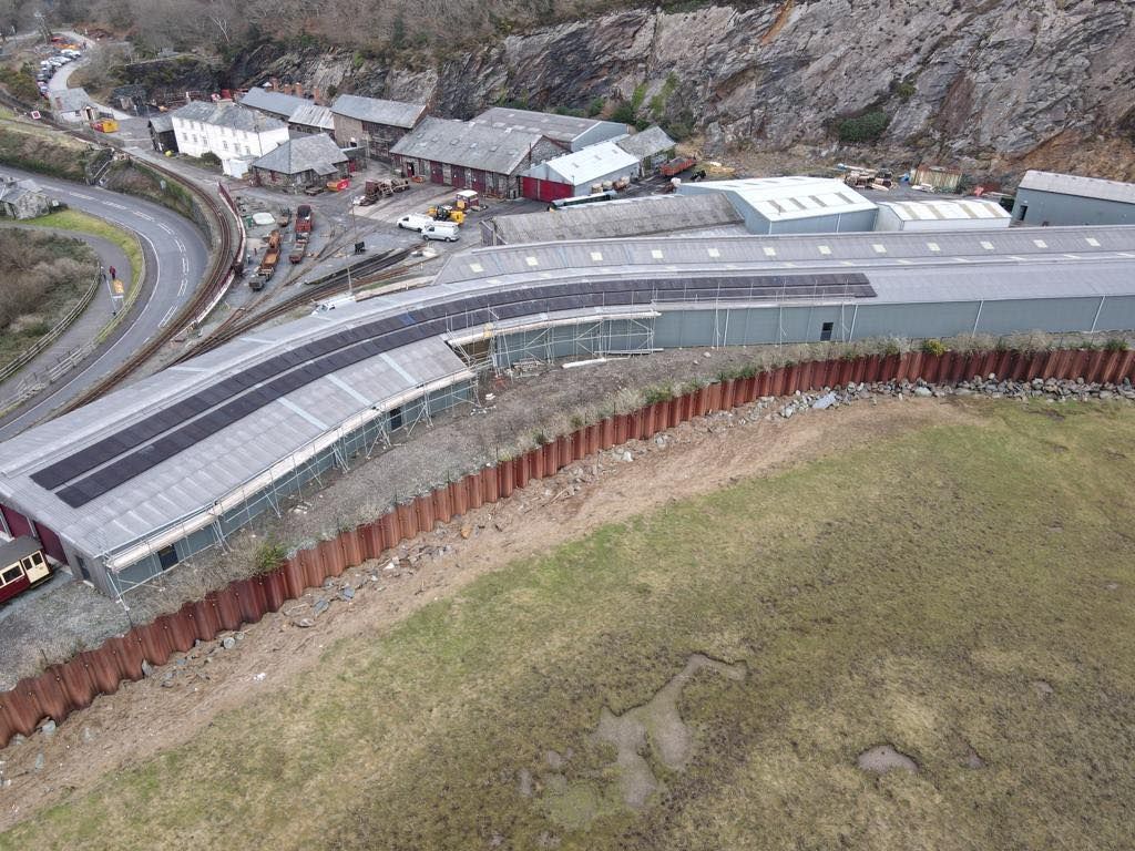 Aerial view of a curved hillside building beside a road, with rocky terrain and construction nearby