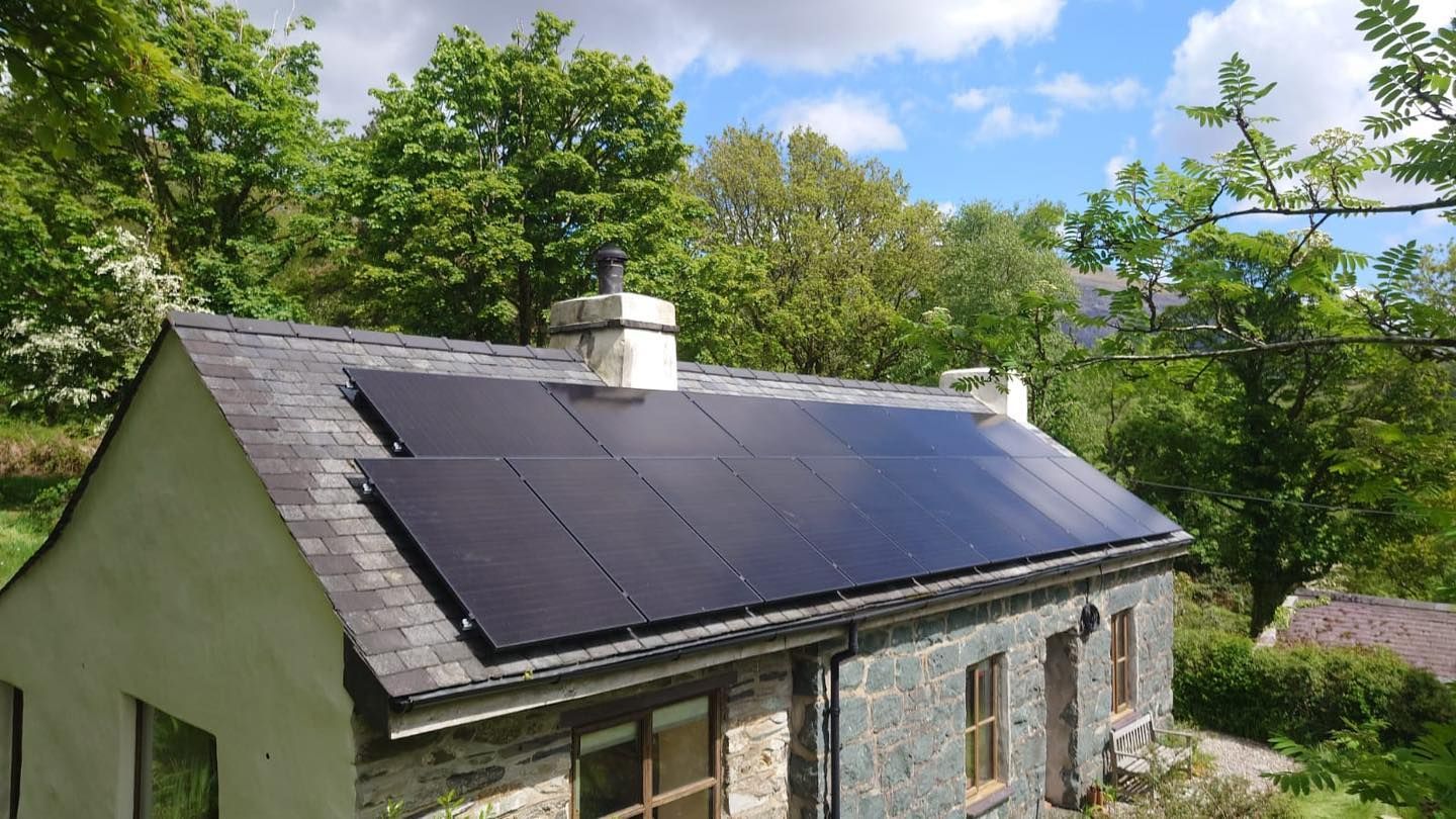 House roof with dark solar panels in a green, wooded setting