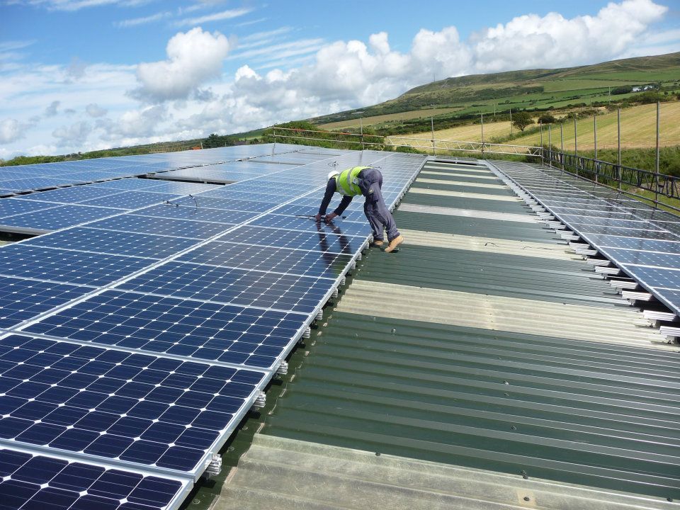 Worker inspecting solar panels on a rooftop under a blue sky