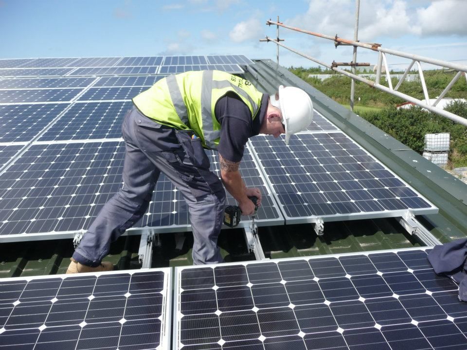 Worker in a hard hat installing rooftop solar panels under a blue sky