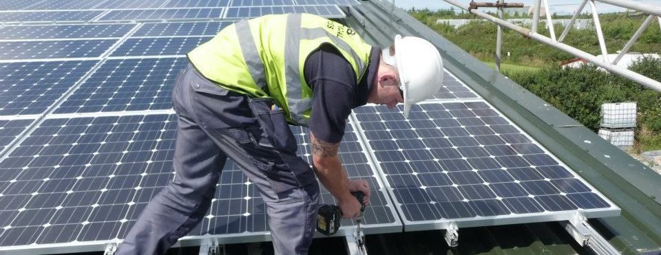 Worker in a hard hat installing solar panels on a rooftop
