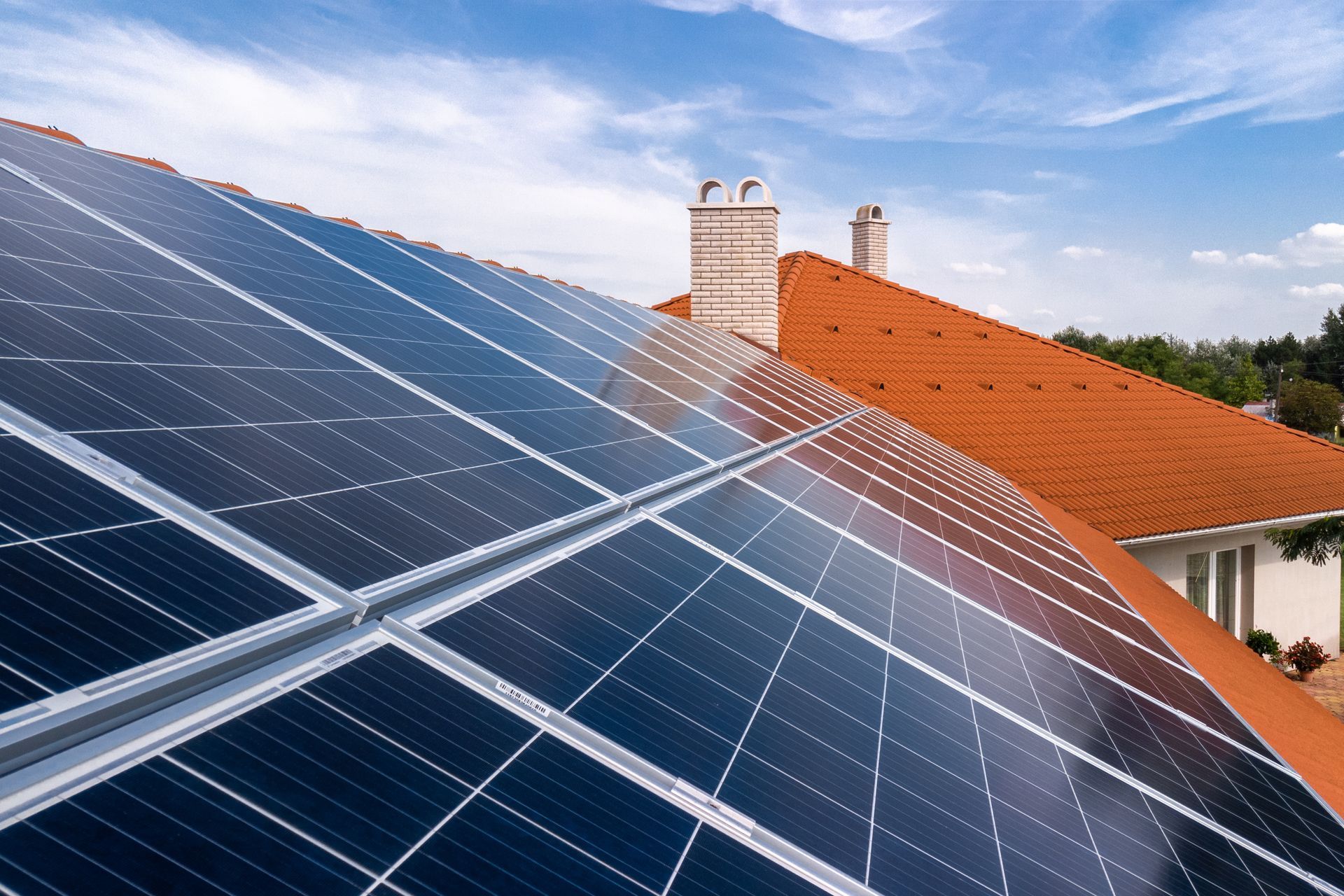 Solar panels on a rooftop beside a red tile house under a blue sky