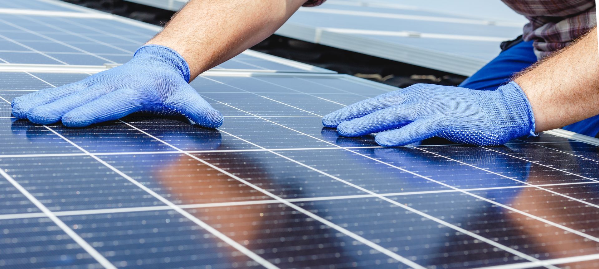 Gloved hands cleaning solar panels with a cloth under bright sunlight
