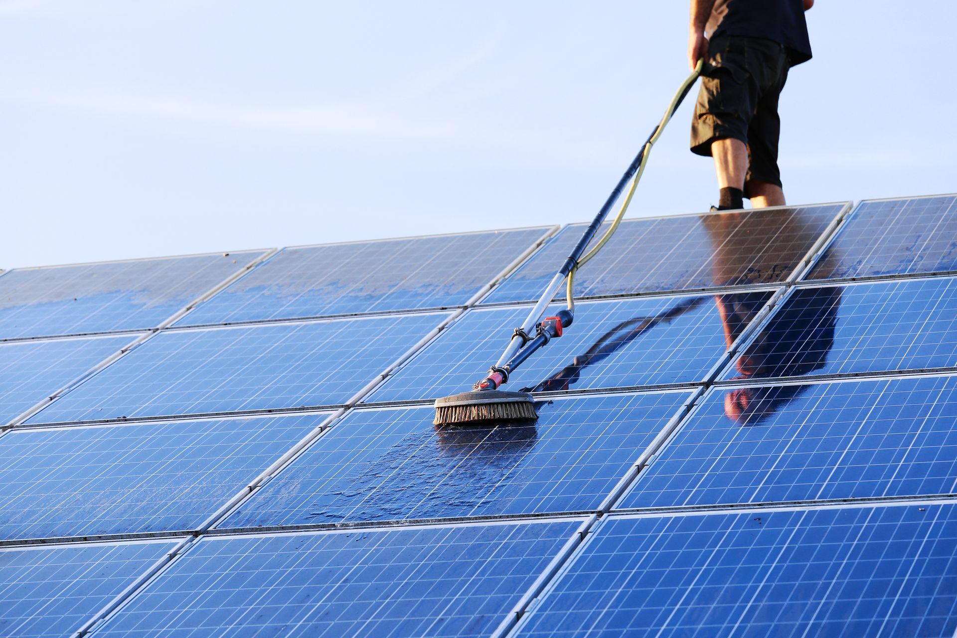 Person cleaning blue solar panels with a brush on a rooftop