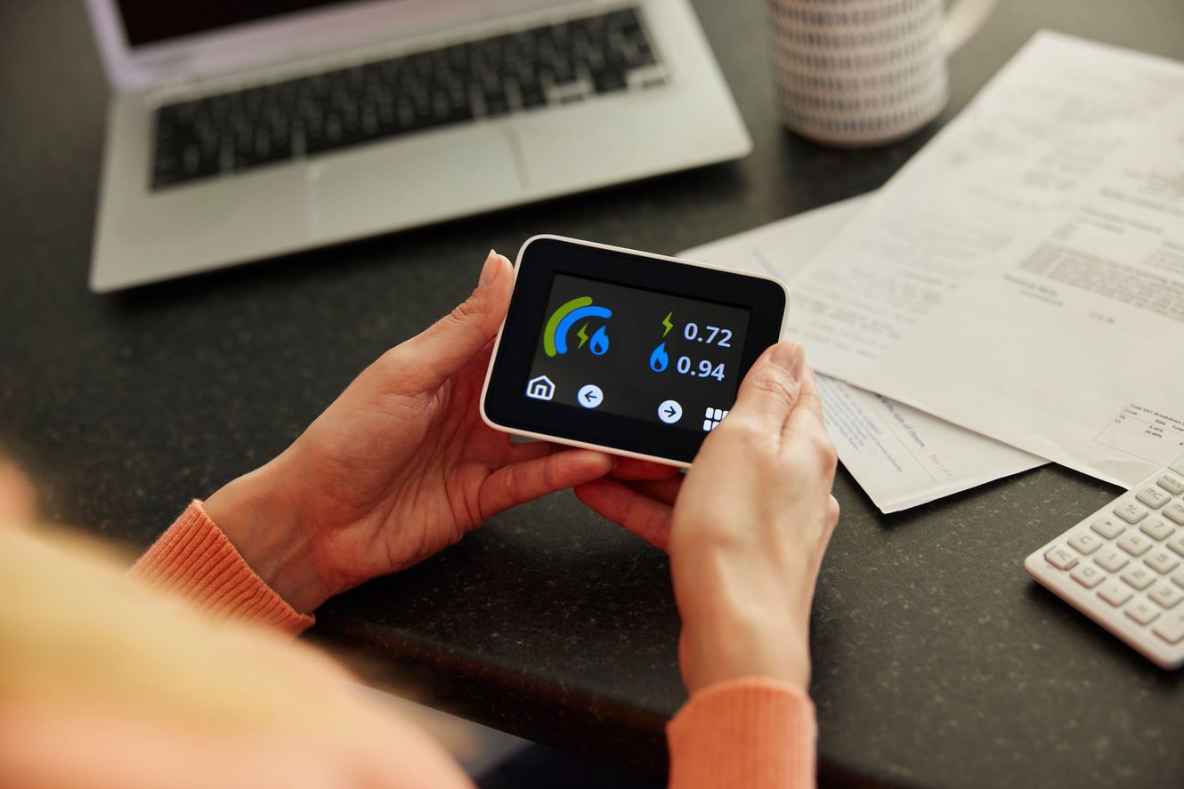 Hands holding a smartphone with dashboard-style app, beside a laptop and papers on a desk