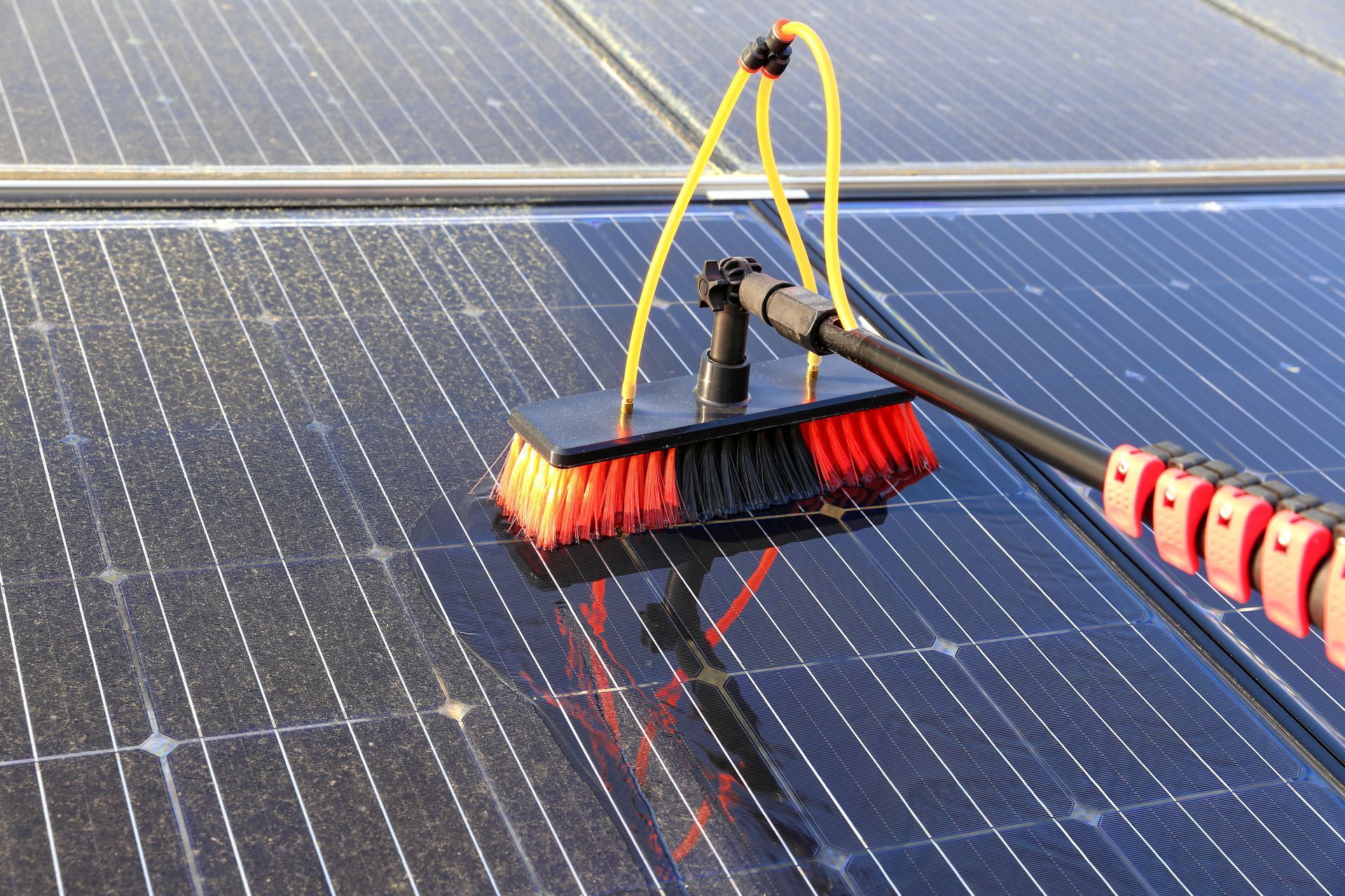 Roof worker using a brush to clean solar panels with water on a rooftop